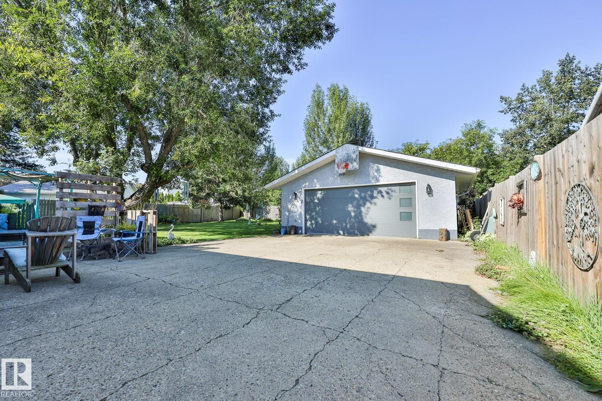 Detached garage with a grey sectional door, concrete driveway, and a wood privacy fence - 8932 187 Street Nw, Edmonton, AB - Outdoor