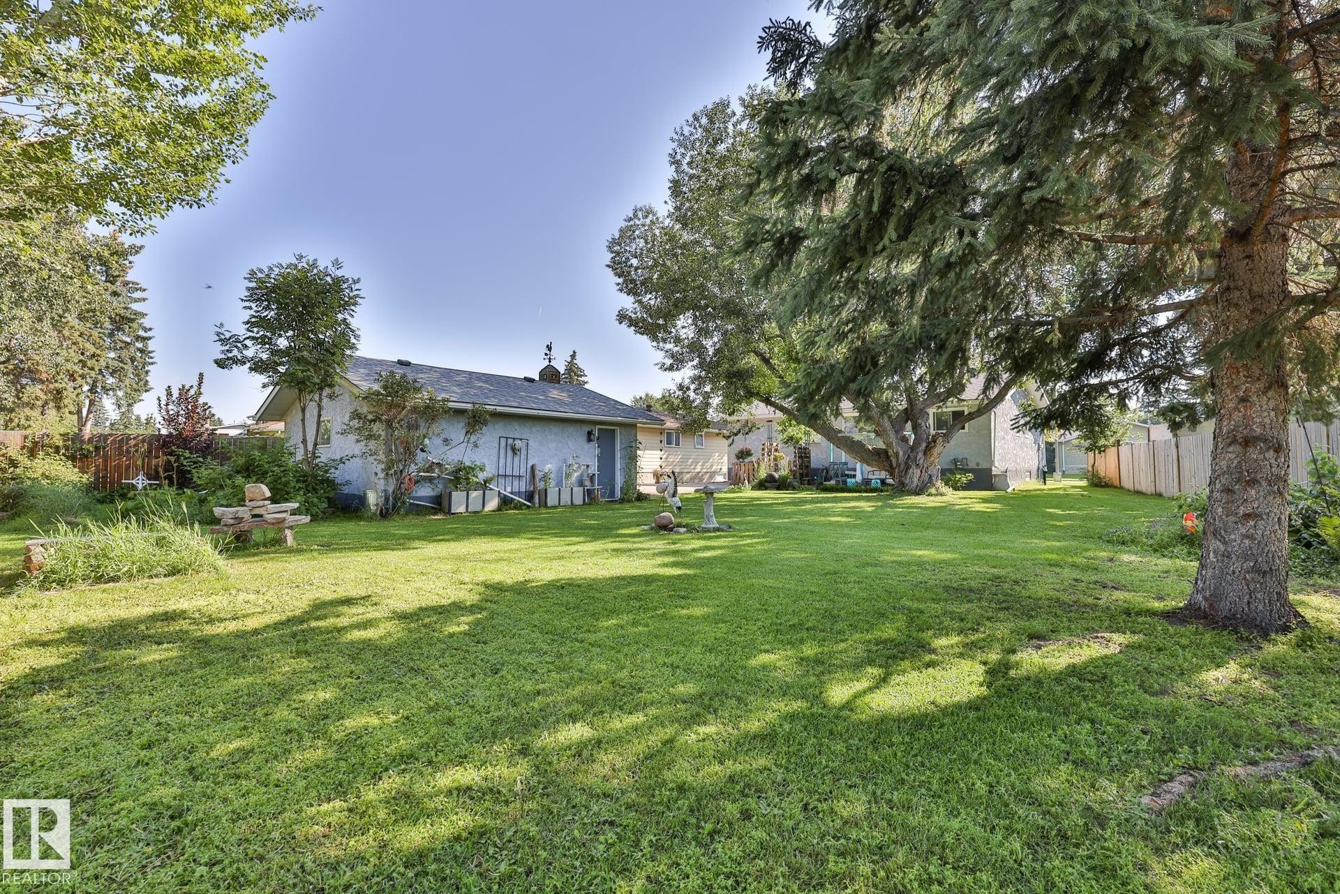 Expansive backyard featuring a lush lawn, mature trees, and a detached structure with a pitched roof - 8932 187 Street Nw, Edmonton, AB - Outdoor