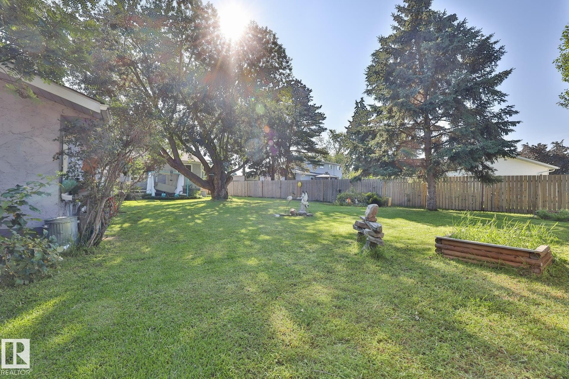 Expansive lawn area, mature trees, wood fence, raised garden bed, and stucco exterior - 8932 187 Street Nw, Edmonton, AB - Outdoor With Backyard