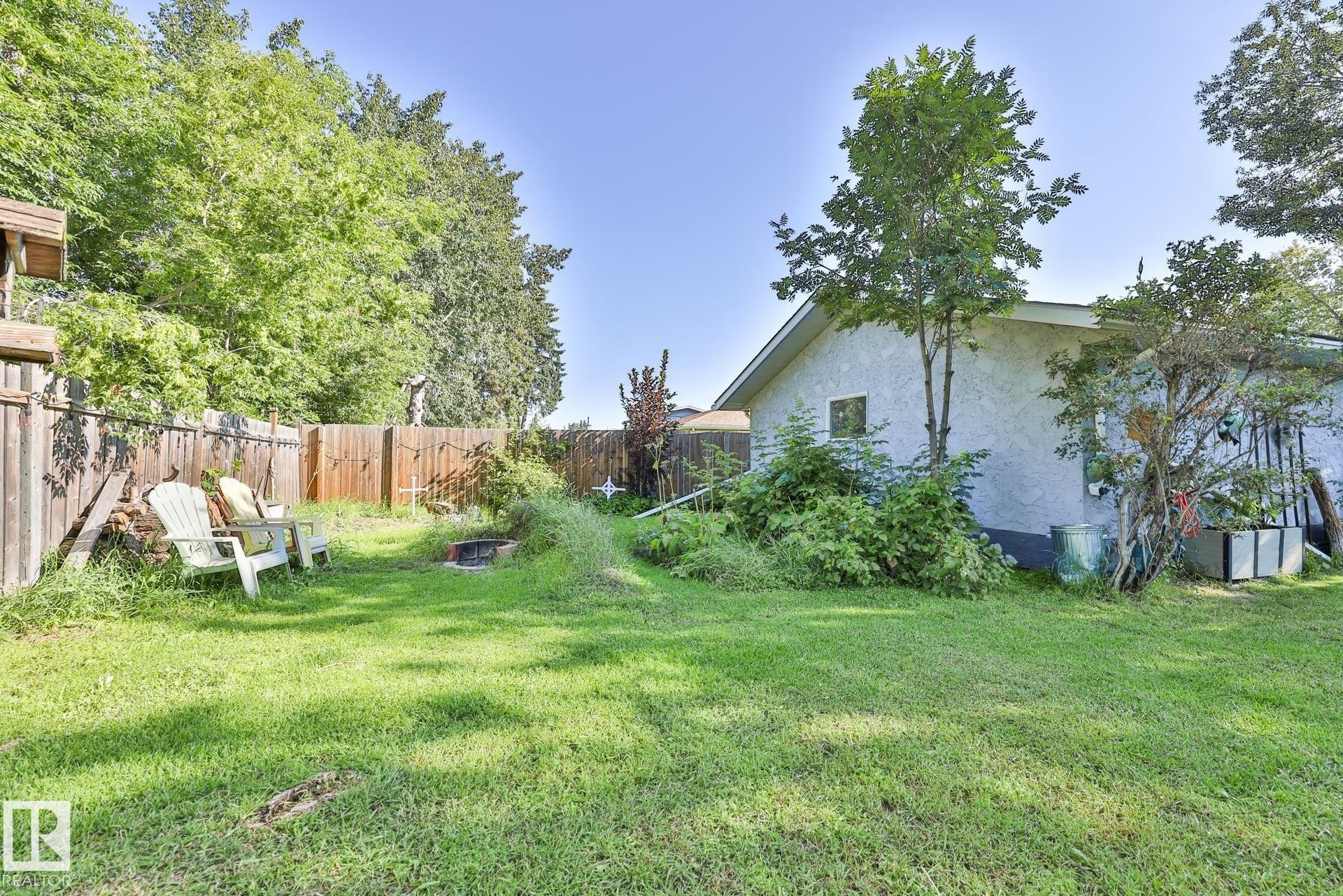 Expansive grassy yard area with a wood privacy fence and mature trees - 8932 187 Street Nw, Edmonton, AB - Outdoor