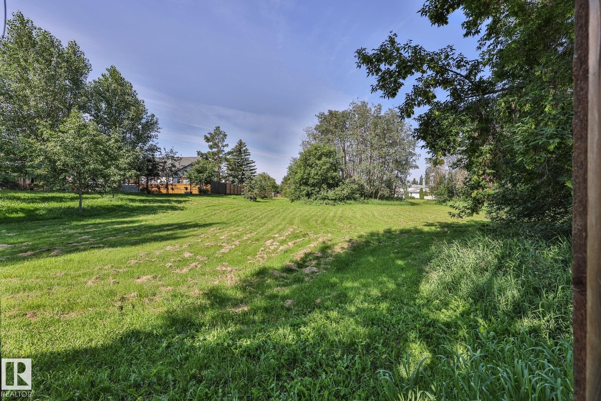 Expansive lot with lush green lawn, mature perimeter trees, and clear blue sky - 8932 187 Street Nw, Edmonton, AB - Outdoor