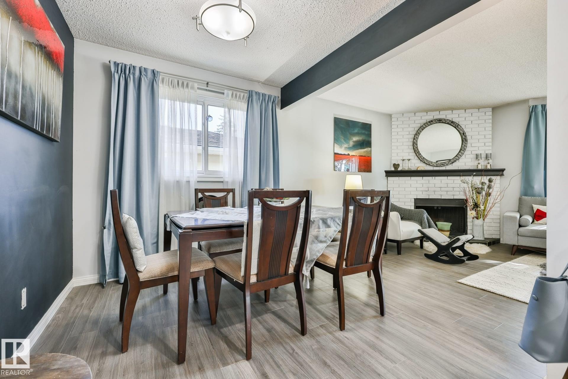 Wood-finish flooring throughout, with a built-in fireplace featuring a white brick surround and black mantle - 8932 187 Street Nw, Edmonton, AB - Indoor Photo Showing Dining Room