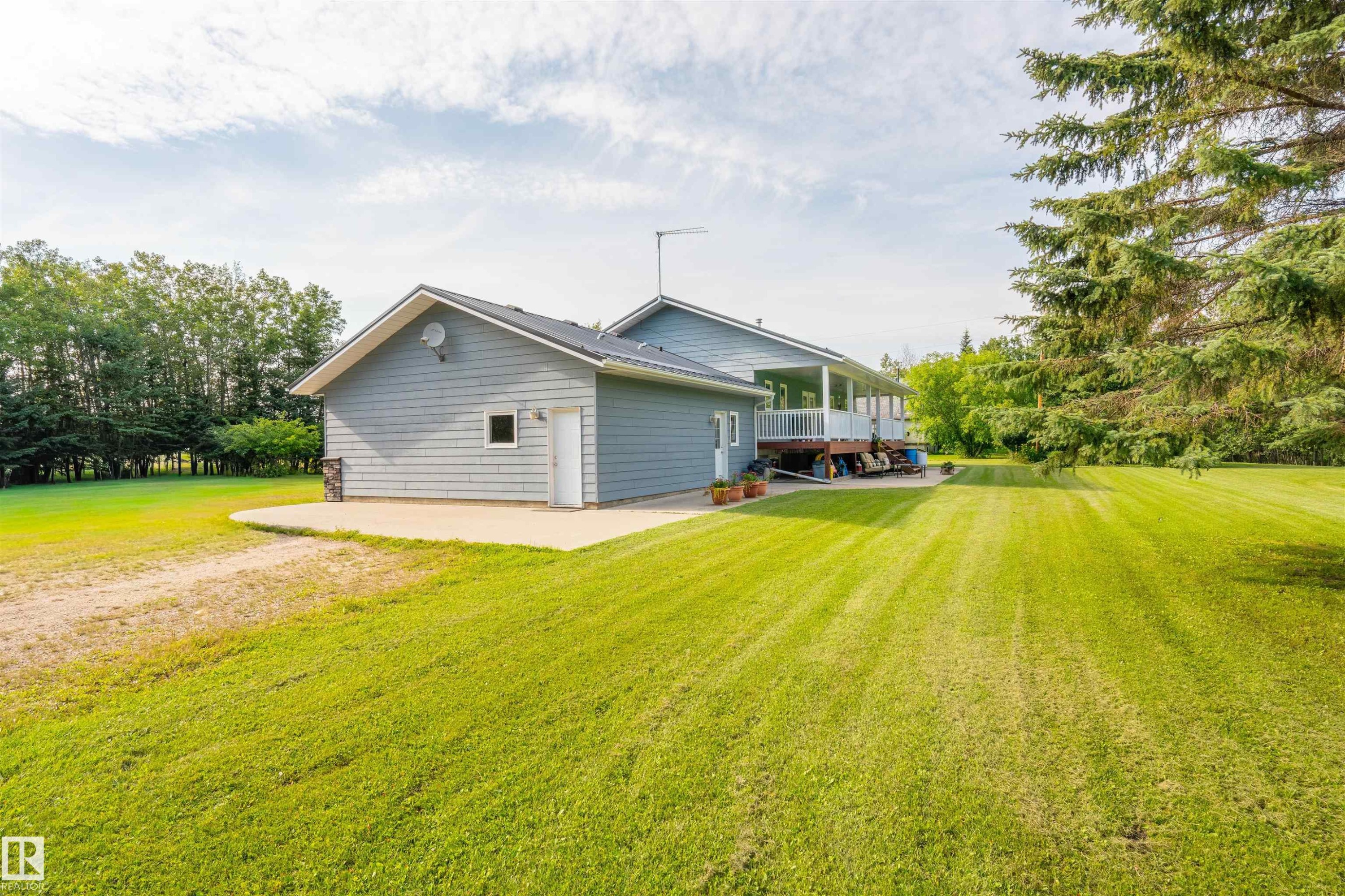 Expansive green lawn surrounds the property, featuring a light blue siding exterior with white trim - 59125 Range Road 102, Rural St. Paul County, AB - Outdoor