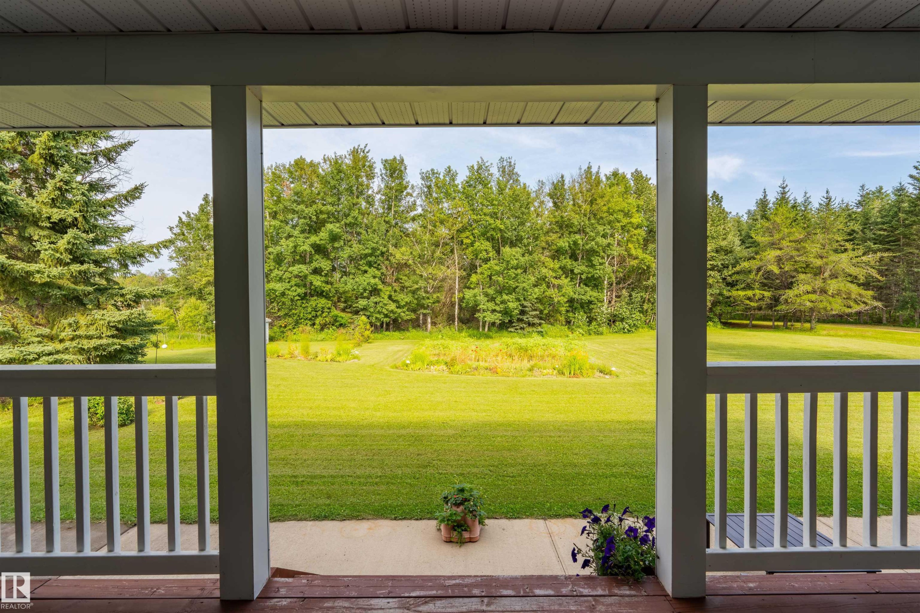 Covered porch with white railings, offering a verdant lawn and mature tree backdrop - 59125 Range Road 102, Rural St. Paul County, AB - Outdoor With Deck Patio Veranda