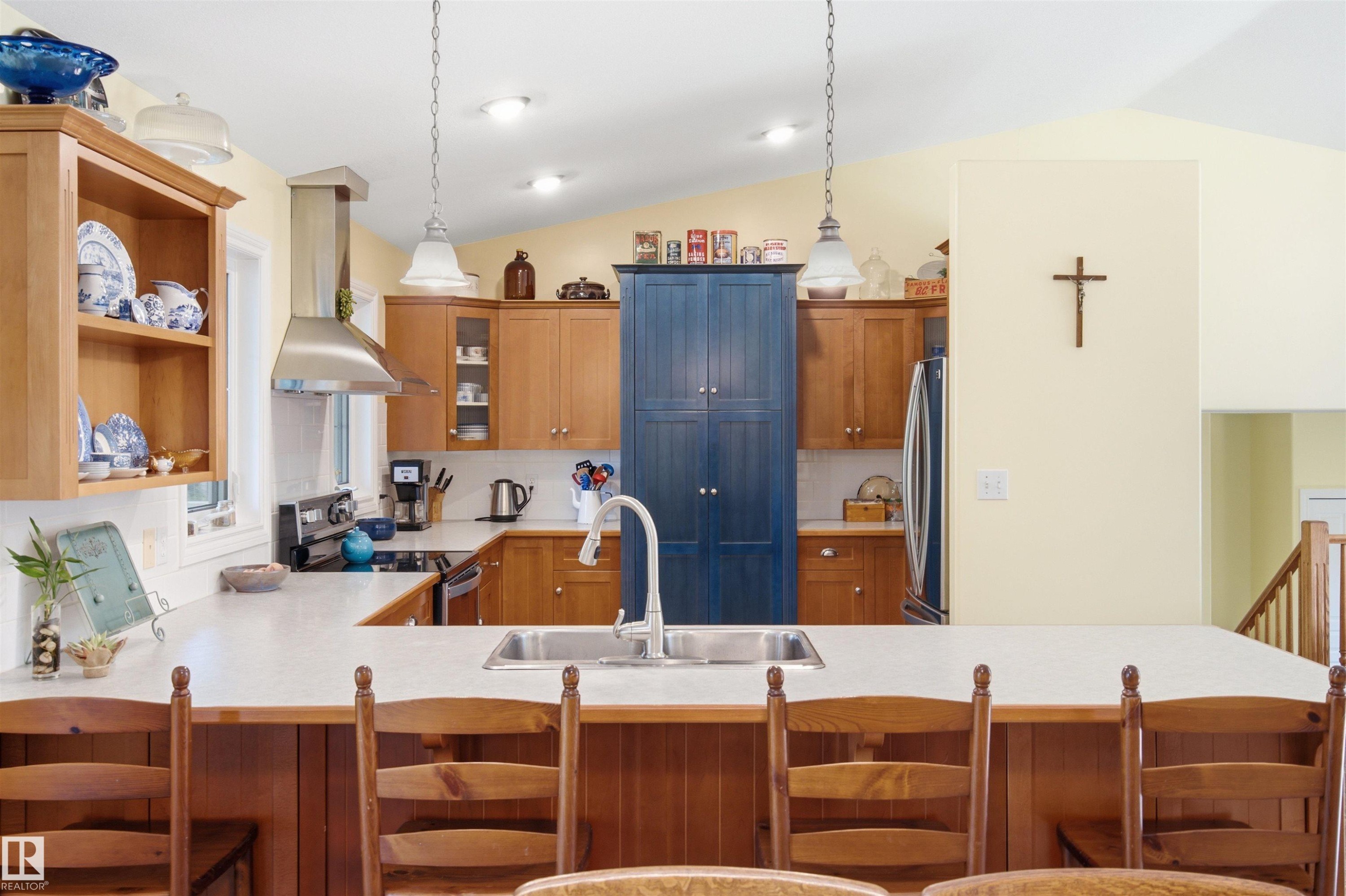Spacious kitchen featuring an expansive island with seating, stainless steel appliances, a range hood, and a built-in pantry cabinet - 59125 Range Road 102, Rural St. Paul County, AB - Indoor Photo Showing Kitchen With Double Sink