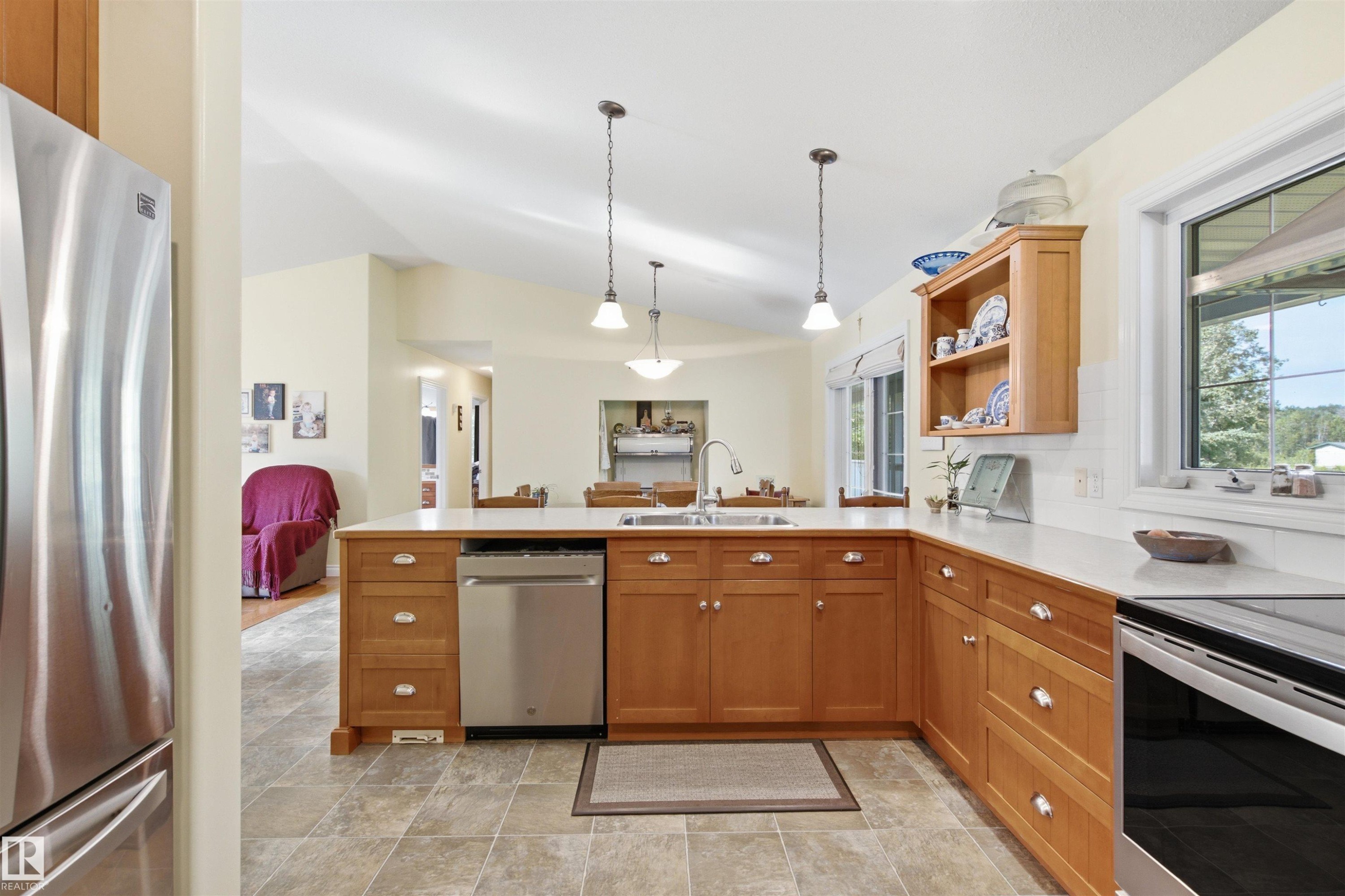 Kitchen featuring light wood cabinetry, light-toned countertops, stainless steel appliances, and a vaulted ceiling - 59125 Range Road 102, Rural St. Paul County, AB - Indoor Photo Showing Kitchen With Double Sink