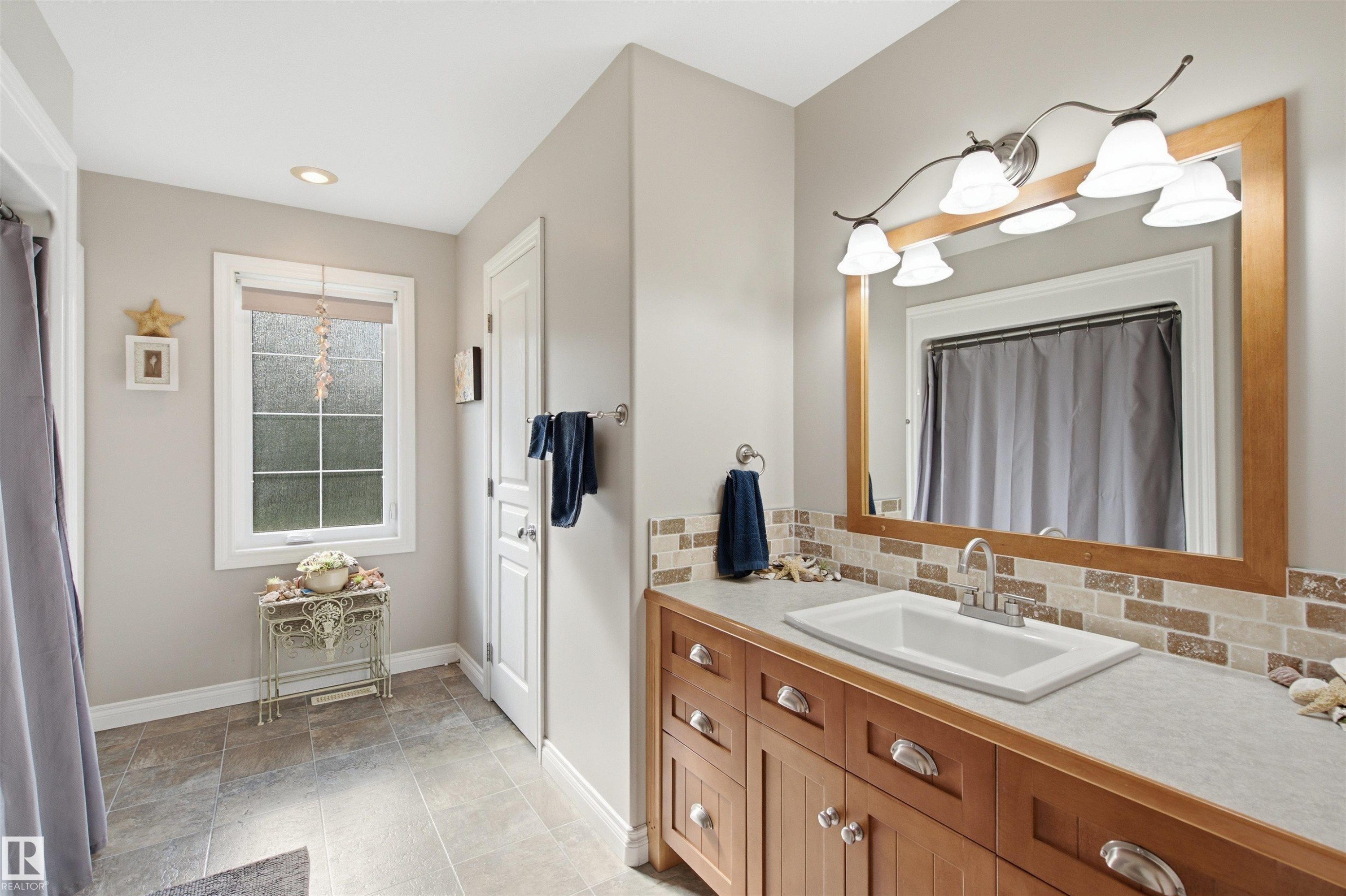 Bathroom featuring a wood vanity with a white rectangular sink, a large framed mirror, and a five-light vanity fixture - 59125 Range Road 102, Rural St. Paul County, AB - Indoor Photo Showing Bathroom