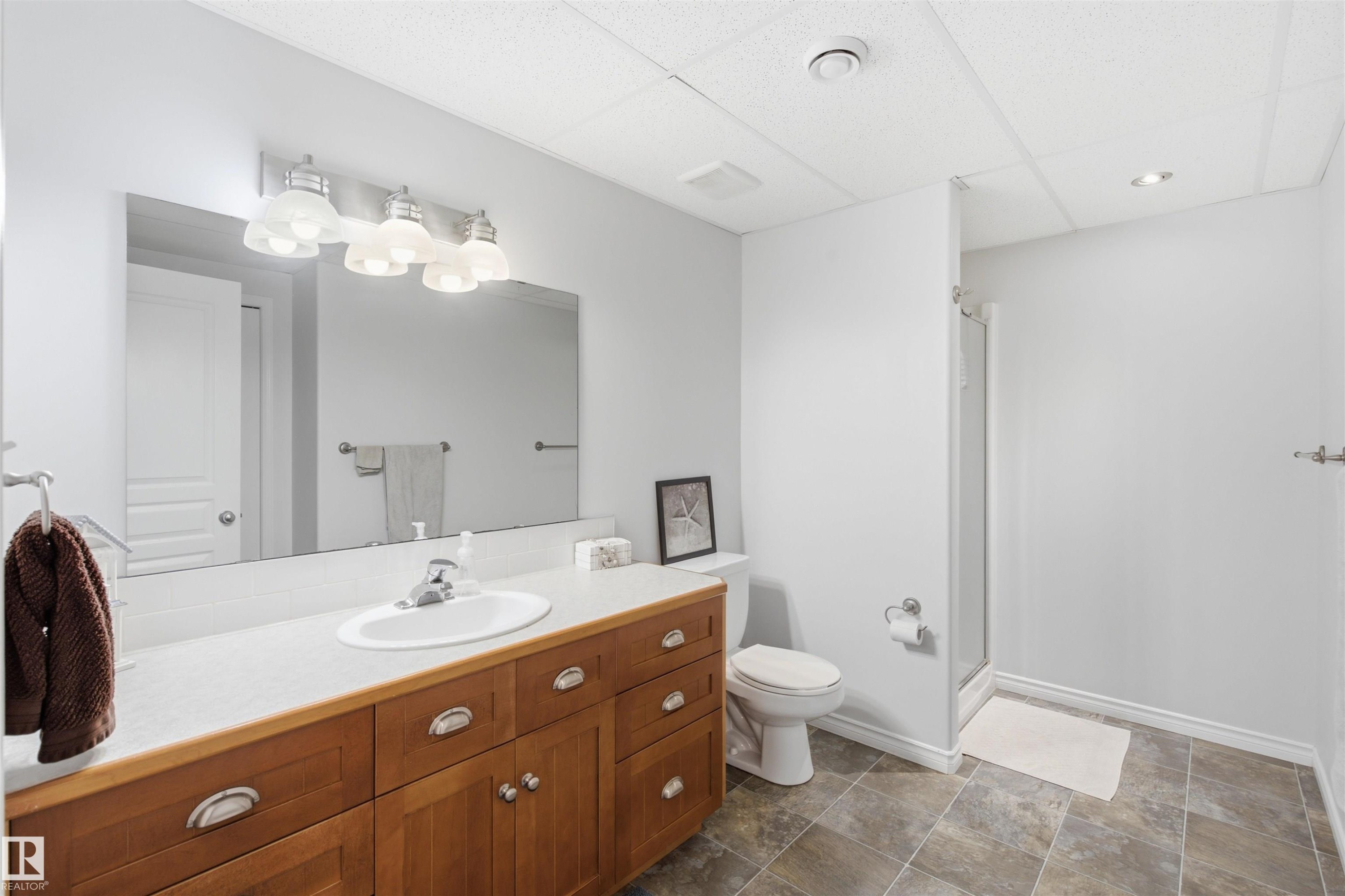 Bathroom featuring a wood-finish vanity with an integrated sink, a large wall mirror, and a four-light fixture - 59125 Range Road 102, Rural St. Paul County, AB - Indoor Photo Showing Bathroom