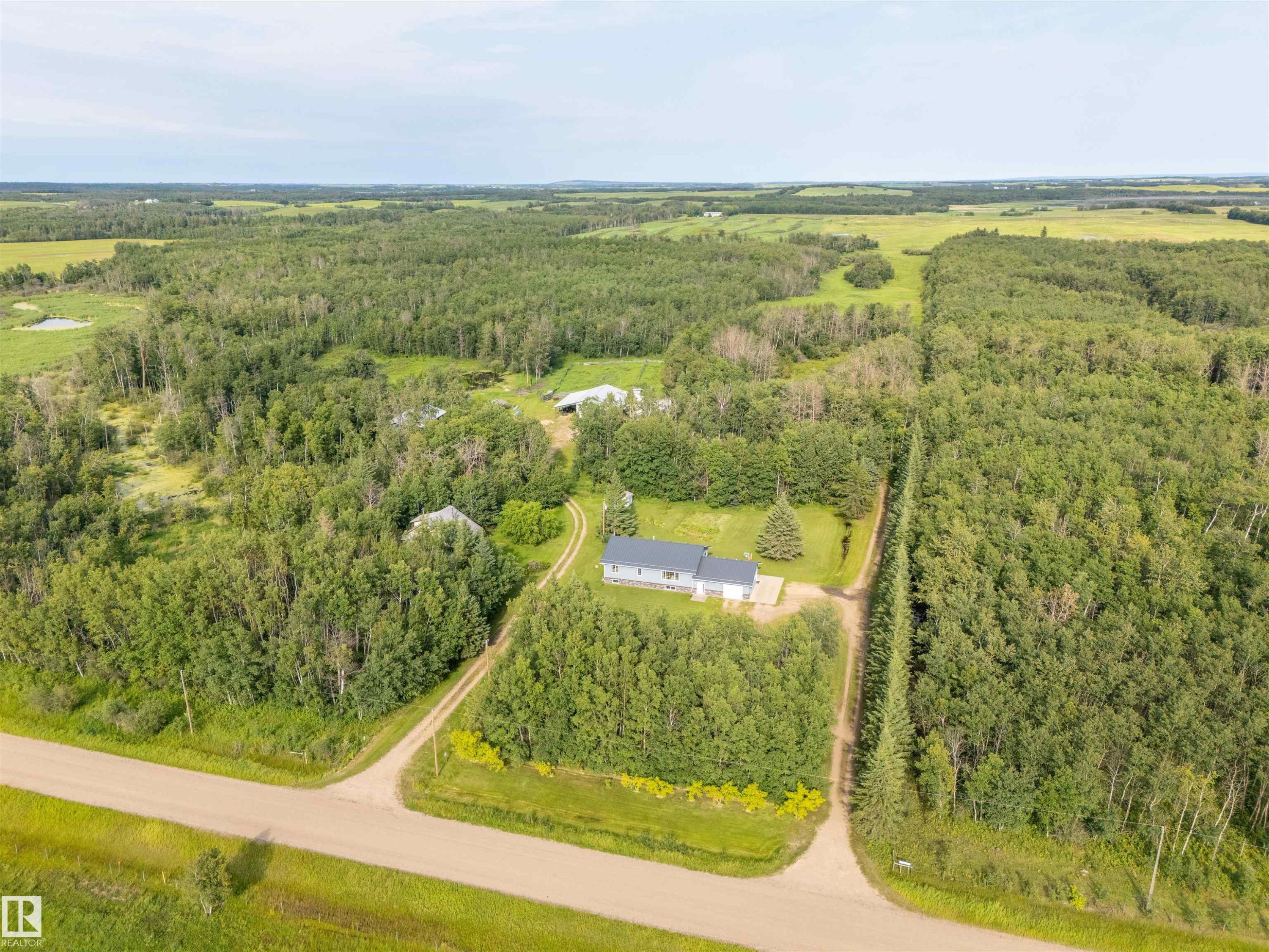Property surrounded by dense mature trees, featuring a light-colored exterior and a dark roof - 59125 Range Road 102, Rural St. Paul County, AB - Outdoor With View