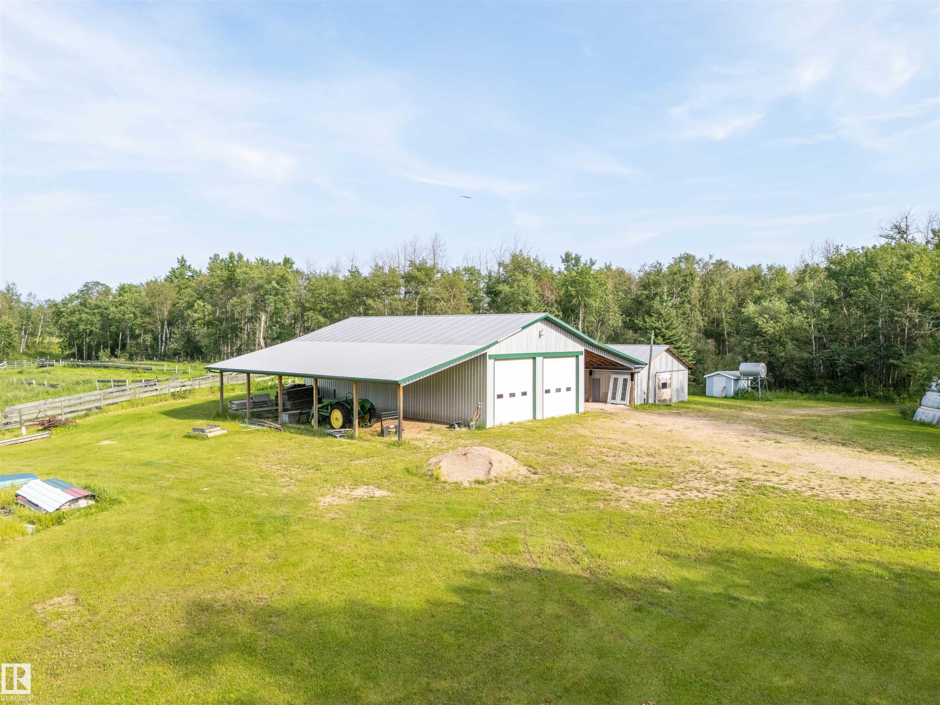 Large Shop structure featuring a light gray metal roof, two white garage doors with green trim, and an attached covered lean-to area - 59125 Range Road 102, Rural St. Paul County, AB - Outdoor