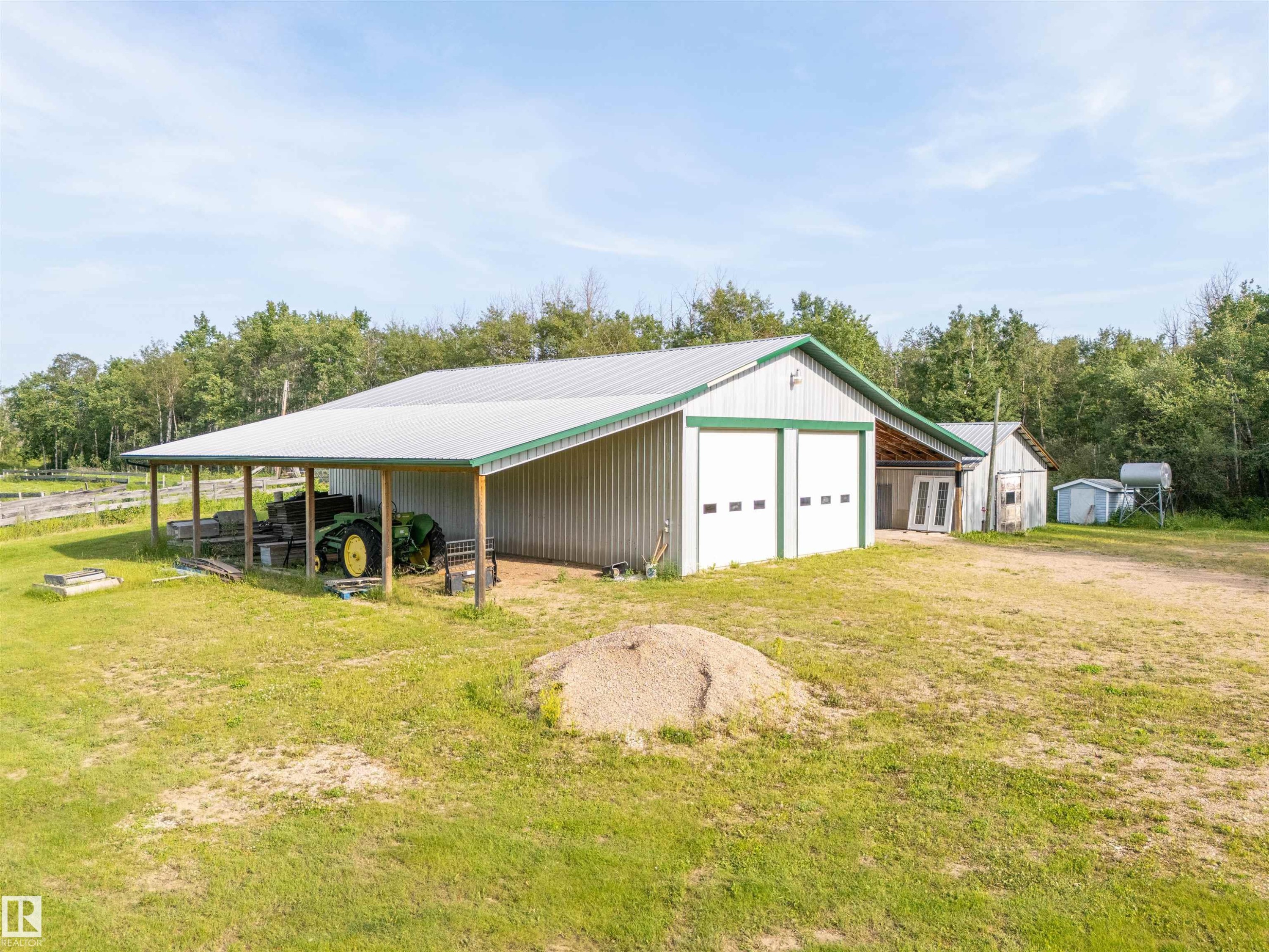 Metal-sided outbuilding with two roll-up garage doors, a covered side extension, and a pitched metal roof - 59125 Range Road 102, Rural St. Paul County, AB - Outdoor With Deck Patio Veranda