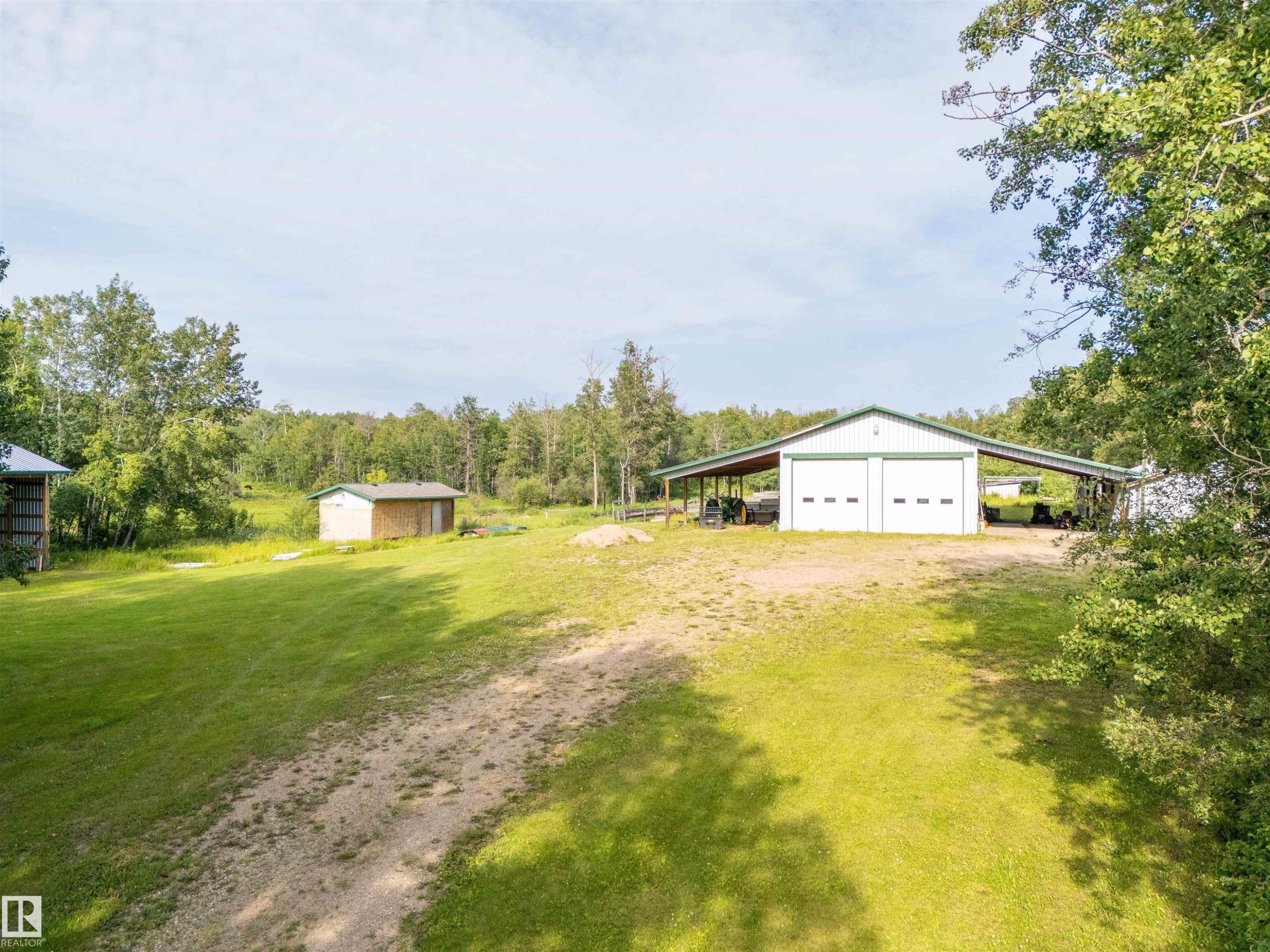 Expansive green space featuring a large shop with two roll-up garage doors, an extended covered carport, and a smaller auxiliary structure - 59125 Range Road 102, Rural St. Paul County, AB - Outdoor