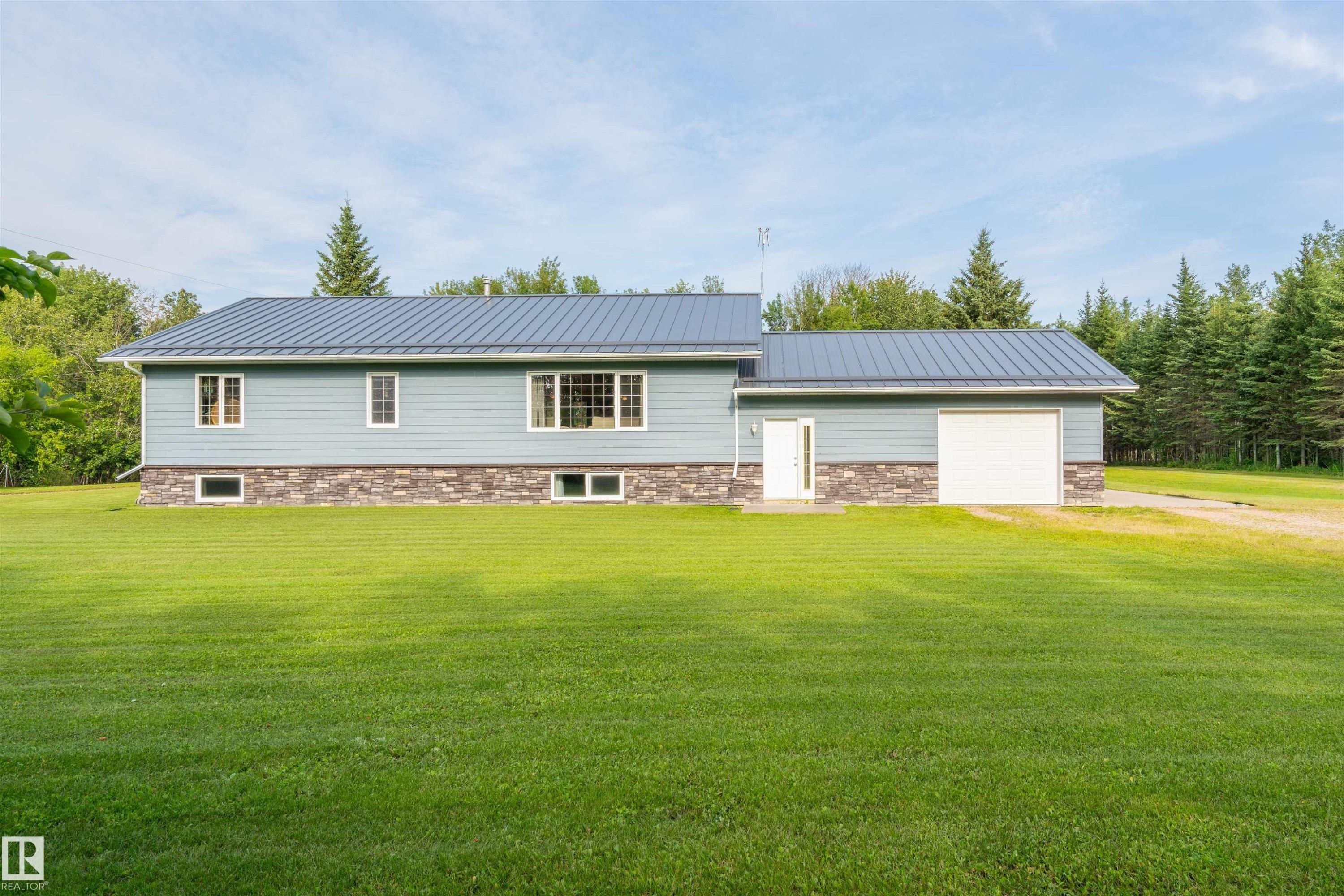 Contemporary residence featuring light blue siding, a metal roof, a stone accent facade, an integrated garage with a white door, and multiple windows - 59125 Range Road 102, Rural St. Paul County, AB - Outdoor