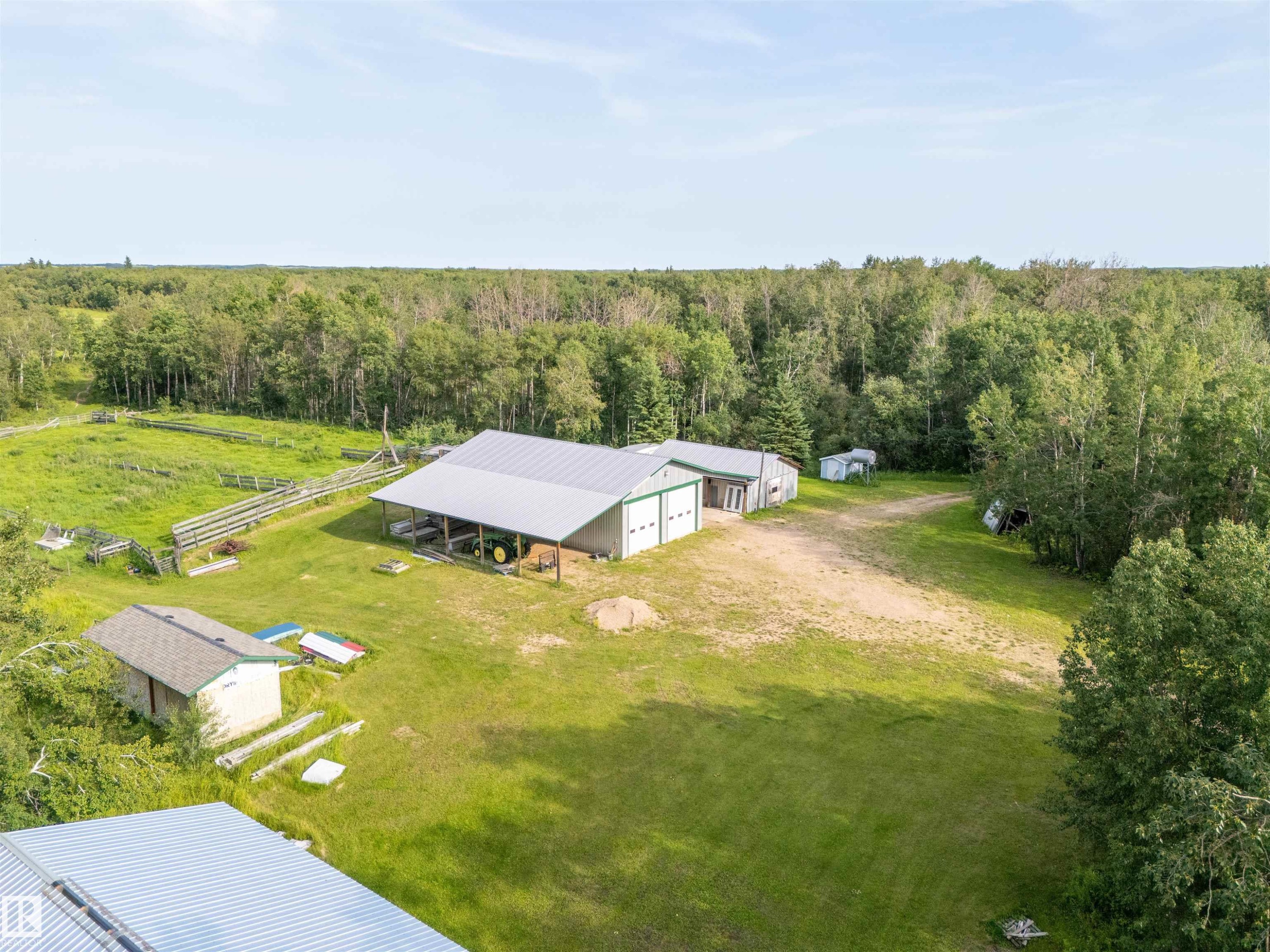 Expansive property featuring multiple outbuildings, including a large structure with dual garage doors and an extended covered area, alongside a smaller shed with a gabled roof - 59125 Range Road 102, Rural St. Paul County, AB - Outdoor With View