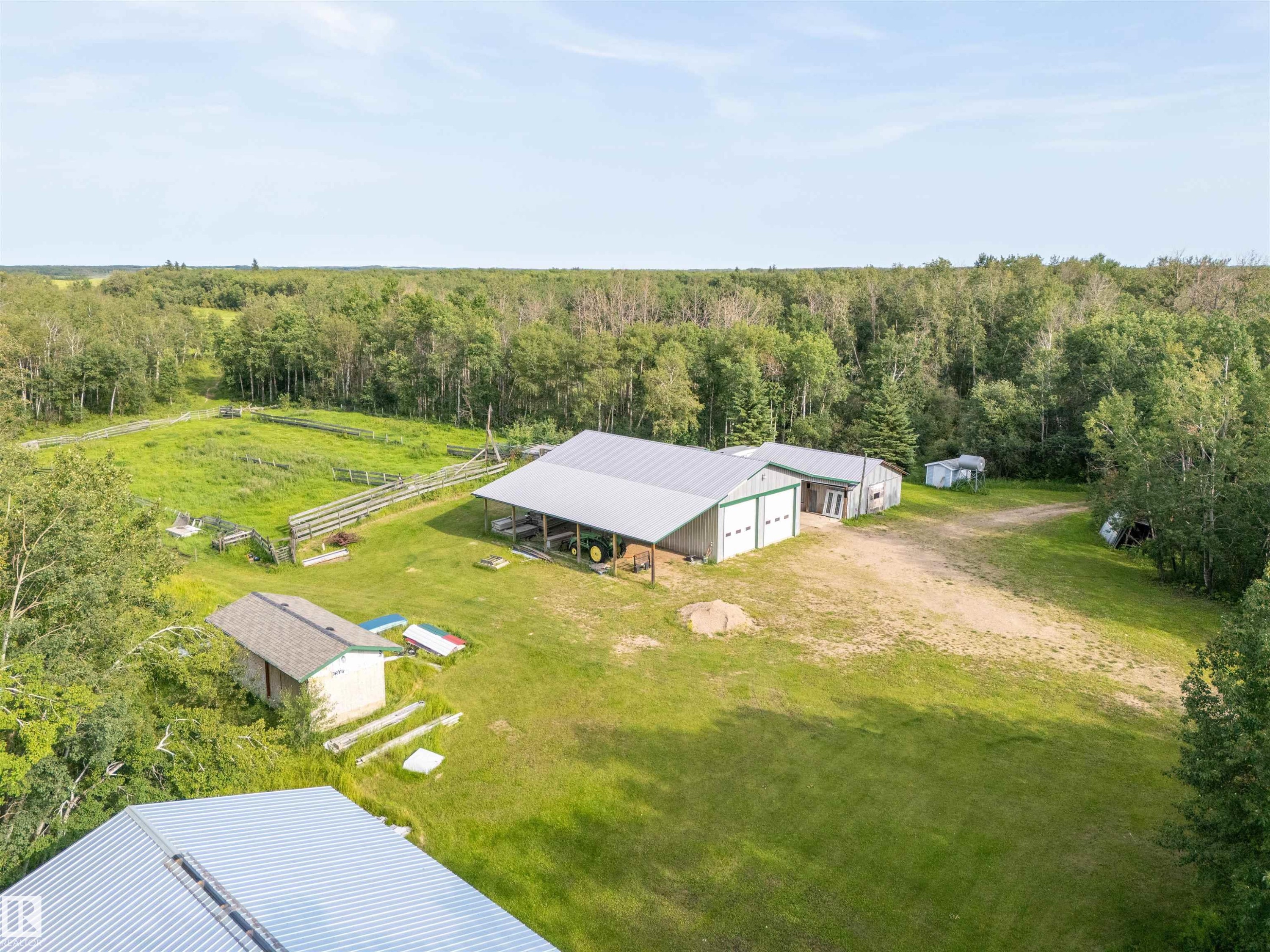Expansive property featuring a large shop with two roll-up garage doors, a covered lean-to, and a separate smaller shed - 59125 Range Road 102, Rural St. Paul County, AB - Outdoor With View