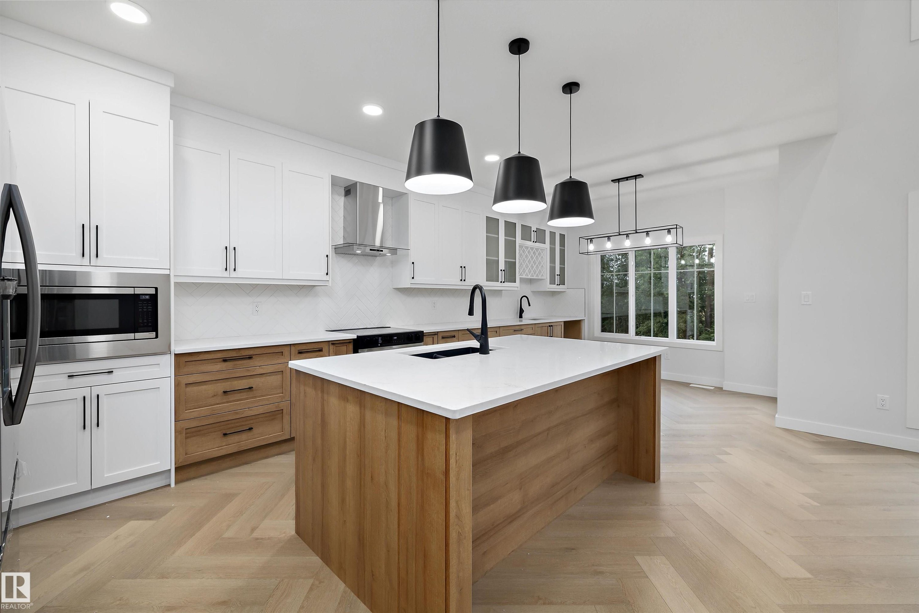 Modern kitchen featuring white cabinetry, light wood-finish flooring, a central island with a white countertop, and stainless steel appliances - 971 Elderberry Landing Nw, Edmonton, AB - Indoor Photo Showing Kitchen