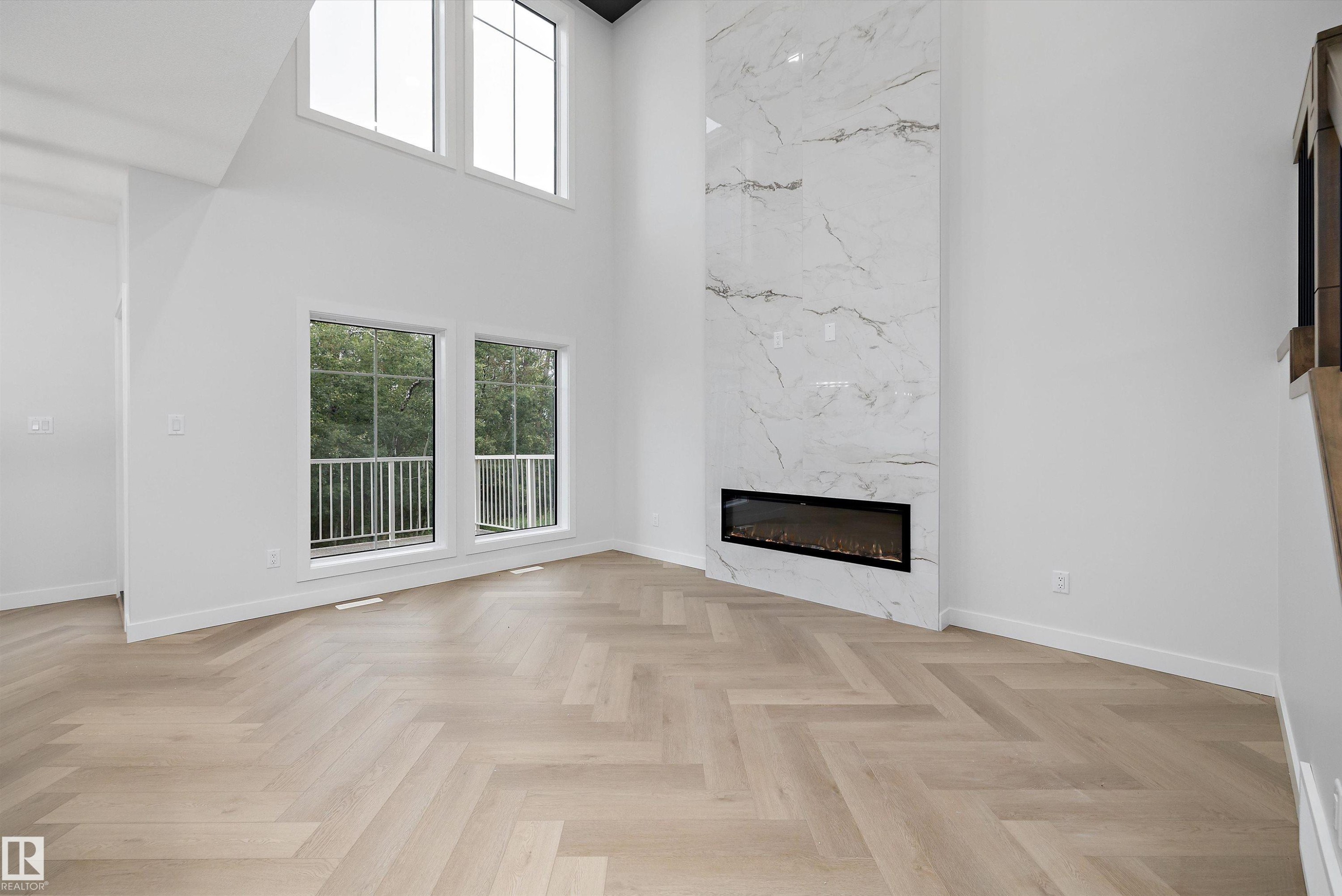 Herringbone wood-finish flooring, two-story accent wall with a linear fireplace, multiple windows, and a railing on the exterior - 971 Elderberry Landing Nw, Edmonton, AB - Indoor Photo Showing Living Room With Fireplace