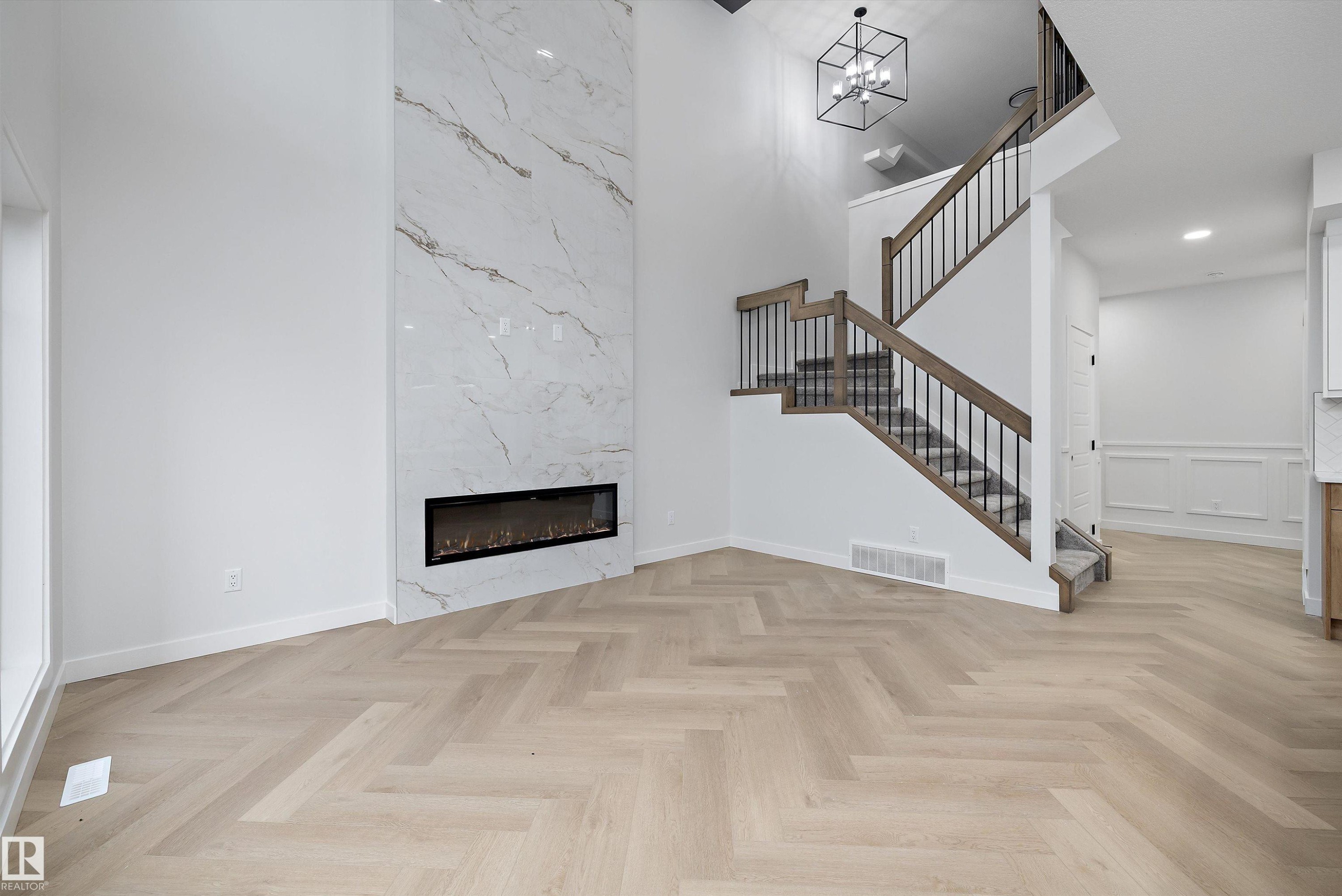 Two-story living area with herringbone wood-finish flooring, a full-height tiled fireplace surround, and a linear electric fireplace - 971 Elderberry Landing Nw, Edmonton, AB - Indoor With Fireplace