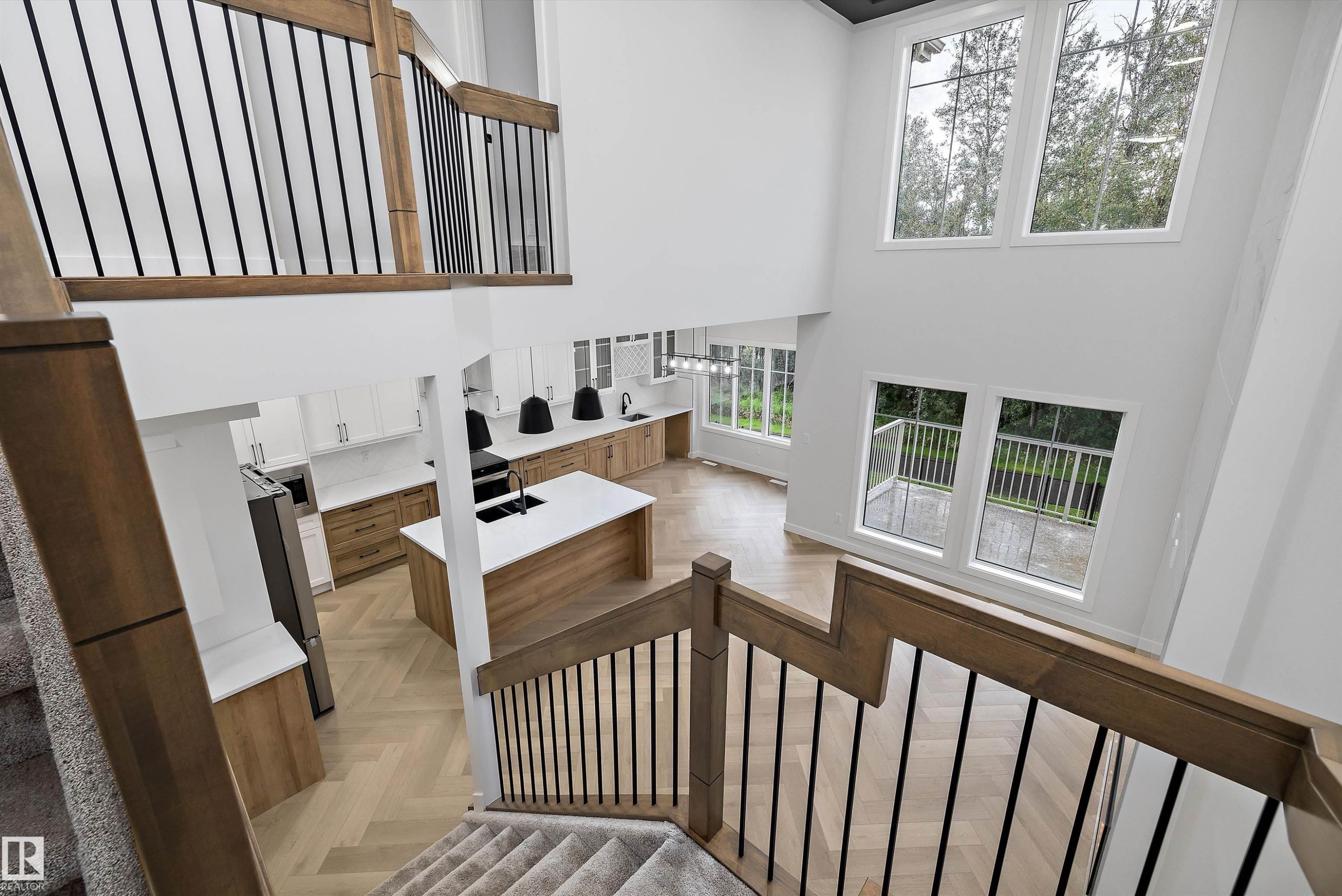 Two-story architectural design, high ceilings, large windows, wood-finish flooring with a herringbone pattern, and a modern kitchen with a central island - 971 Elderberry Landing Nw, Edmonton, AB - Indoor Photo Showing Other Room