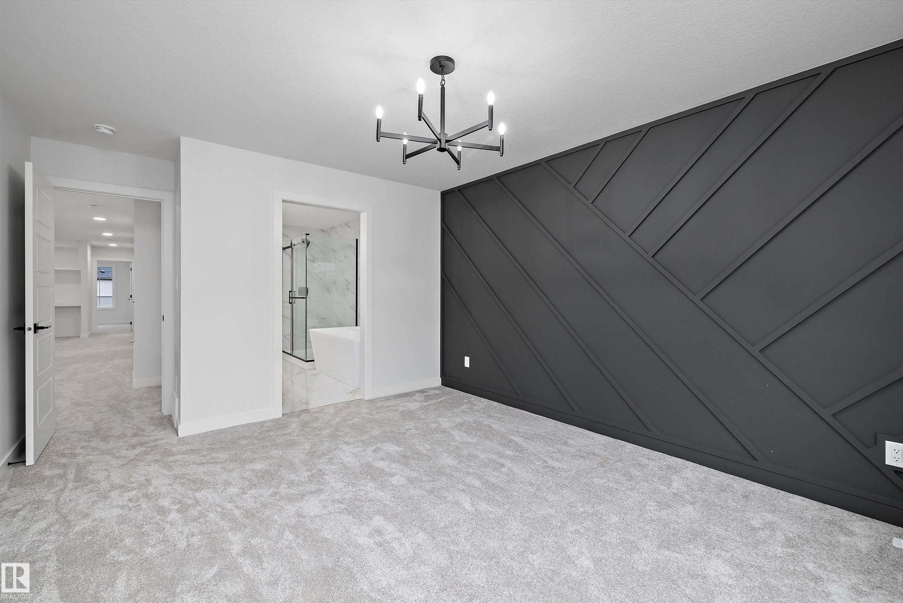 Accent wall with geometric paneling, contemporary chandelier, light-toned carpeting, and a full bathroom with a shower-over-tub combination - 971 Elderberry Landing Nw, Edmonton, AB - Indoor Photo Showing Other Room