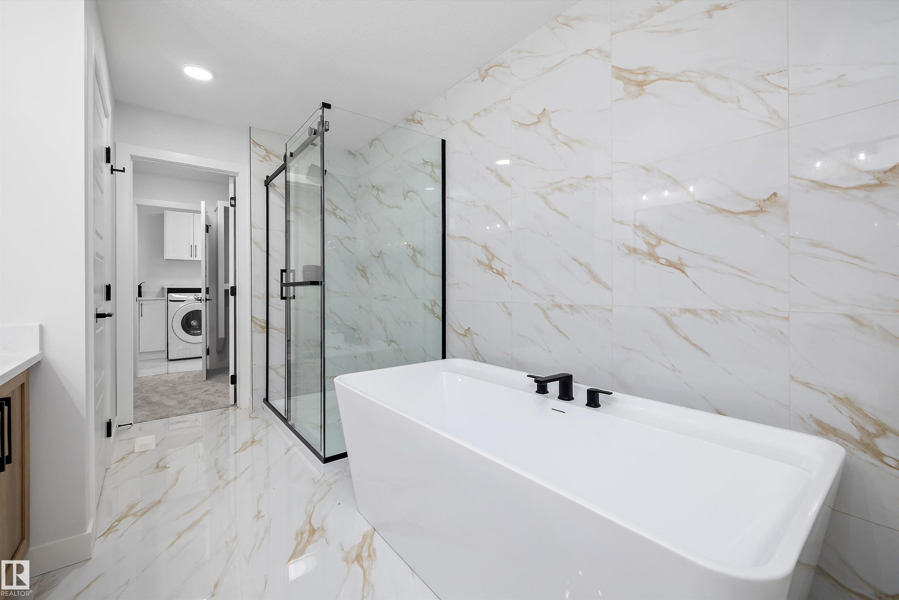Freestanding soaking tub with matte black fixtures, glass-enclosed shower, and large format wall and floor tiling - 971 Elderberry Landing Nw, Edmonton, AB - Indoor Photo Showing Bathroom