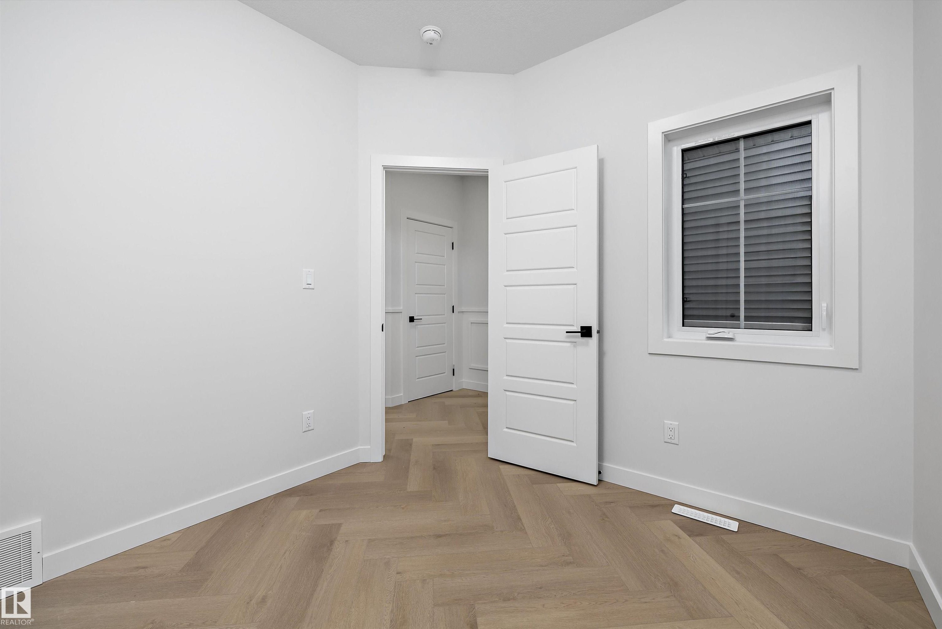 Herringbone wood-finish flooring, white paneled interior doors, white trim, and a window with blinds - 971 Elderberry Landing Nw, Edmonton, AB - Indoor Photo Showing Other Room