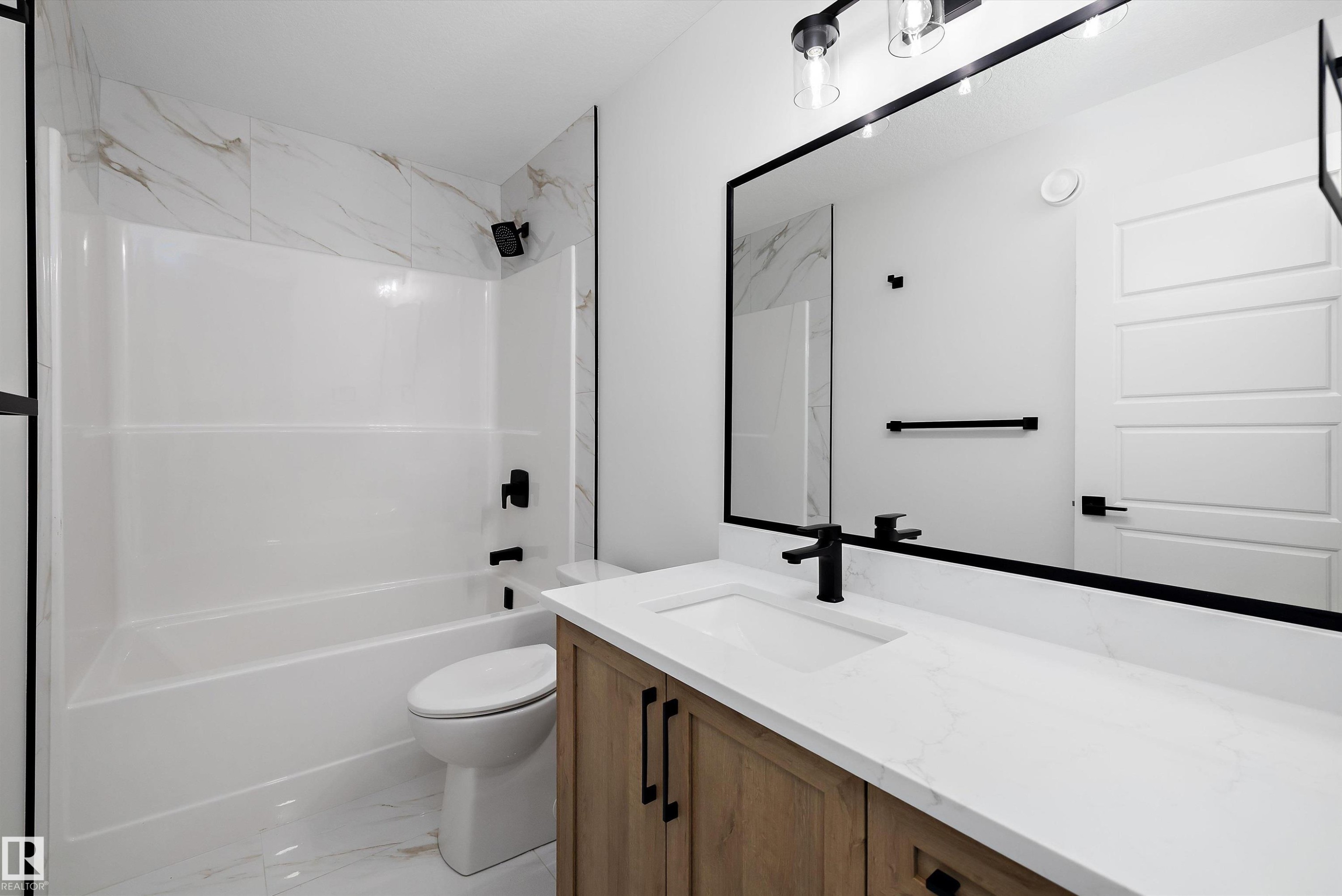 Bathroom featuring a built-in tub with a tile surround, wood-finish vanity with a white countertop, undermount sink, and matte black hardware - 971 Elderberry Landing Nw, Edmonton, AB - Indoor Photo Showing Bathroom