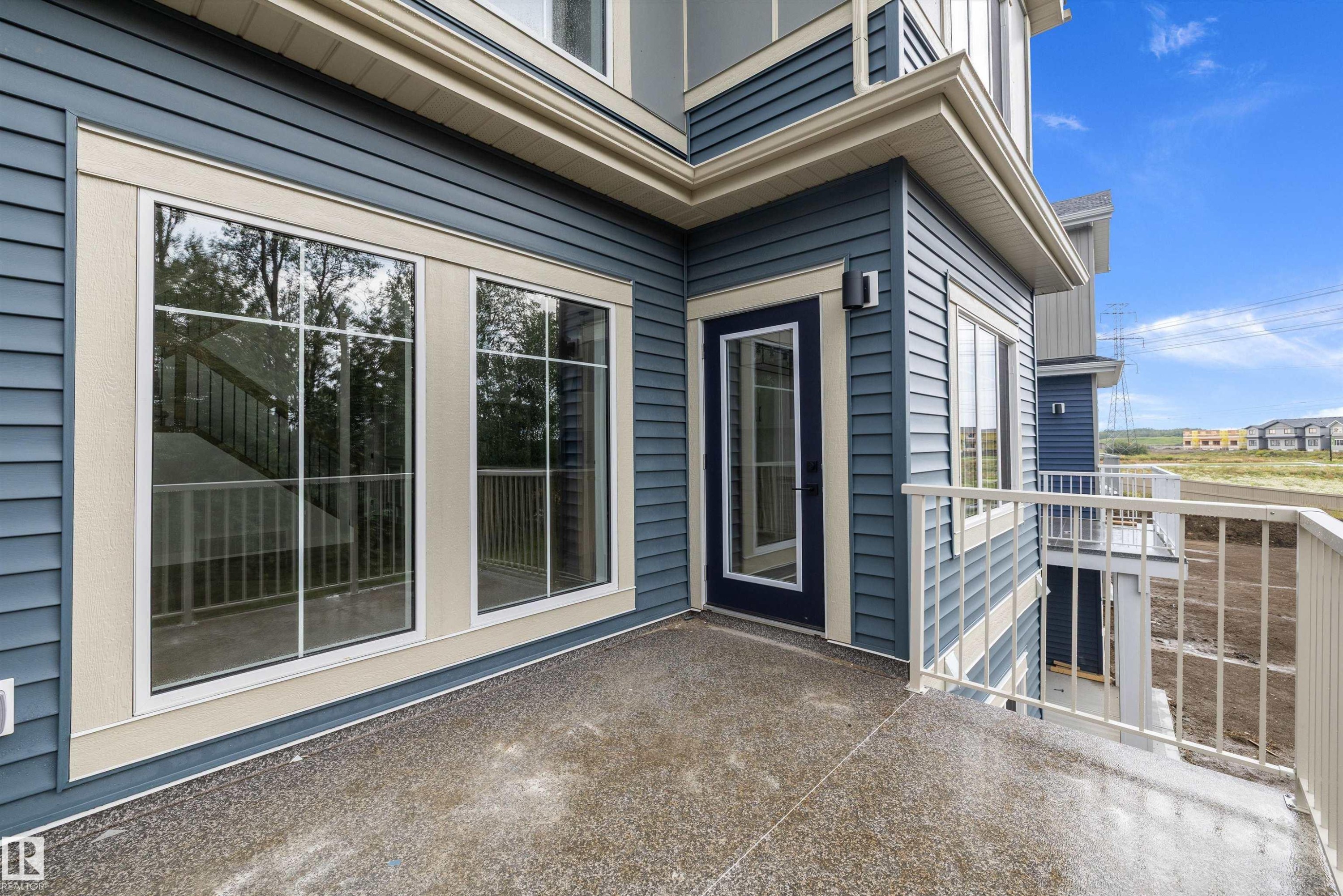 Exterior balcony with a textured concrete surface and white metal railings, featuring blue horizontal siding and contrasting cream trim - 971 Elderberry Landing Nw, Edmonton, AB - Outdoor With Deck Patio Veranda With Exterior