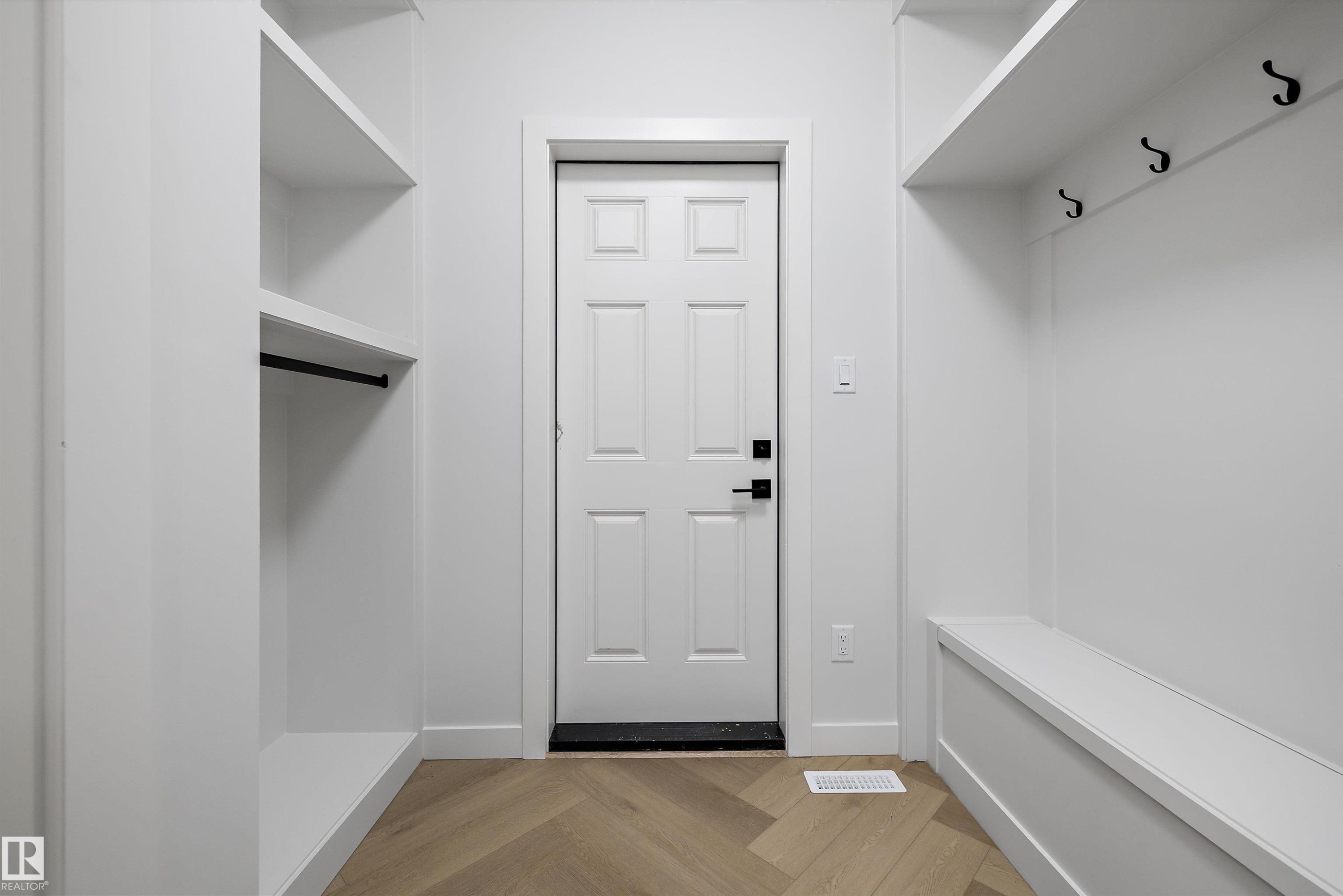 Entryway featuring wood-finish flooring with a herringbone pattern, a paneled door with black hardware, built-in shelving, a built-in bench, and black coat hooks - 971 Elderberry Landing Nw, Edmonton, AB - Indoor