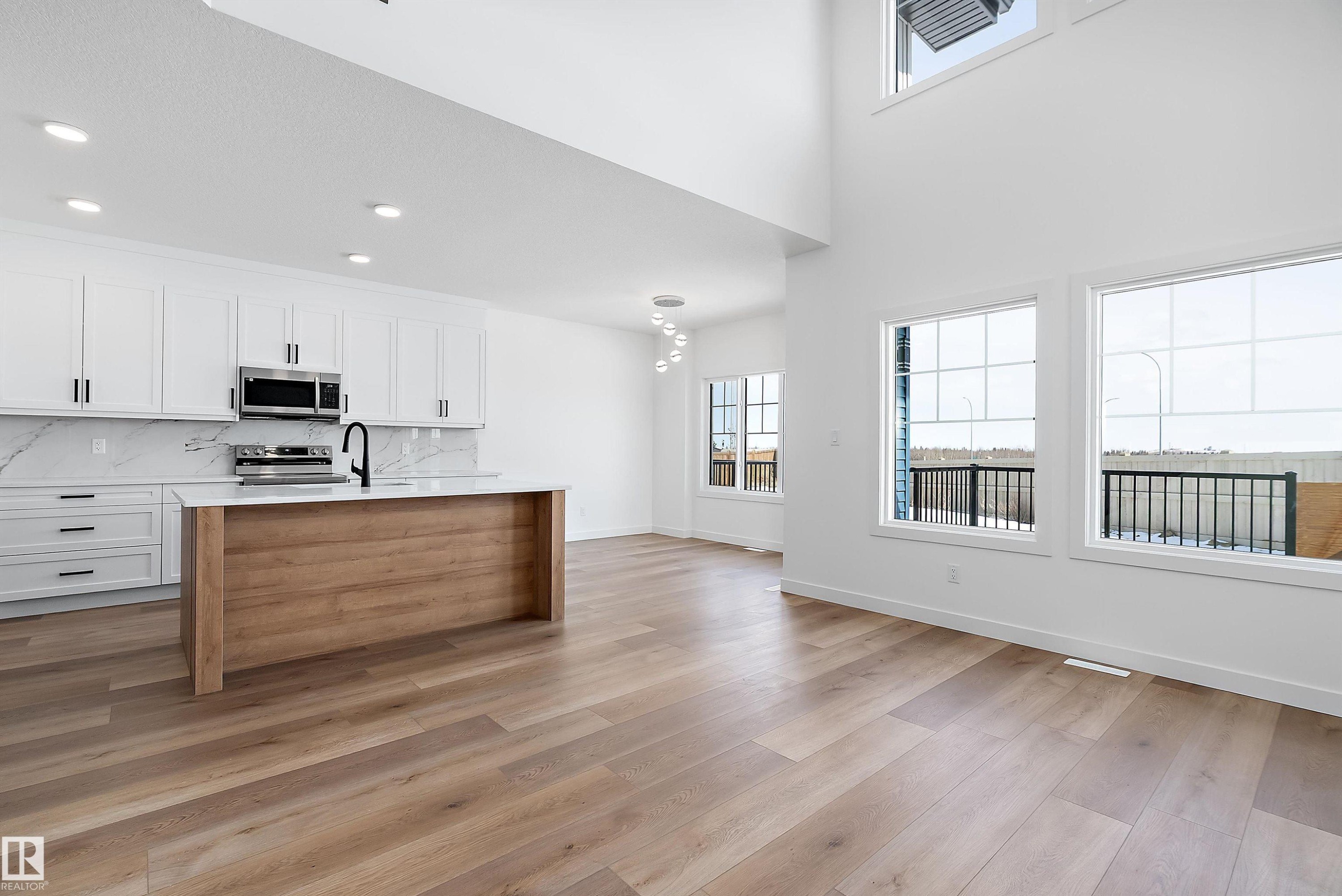 Vaulted ceiling, wood-finish flooring, white cabinetry, integrated kitchen island, and stainless steel appliances - 1763 Crossbill Loop Nw, Edmonton, AB - Indoor Photo Showing Kitchen