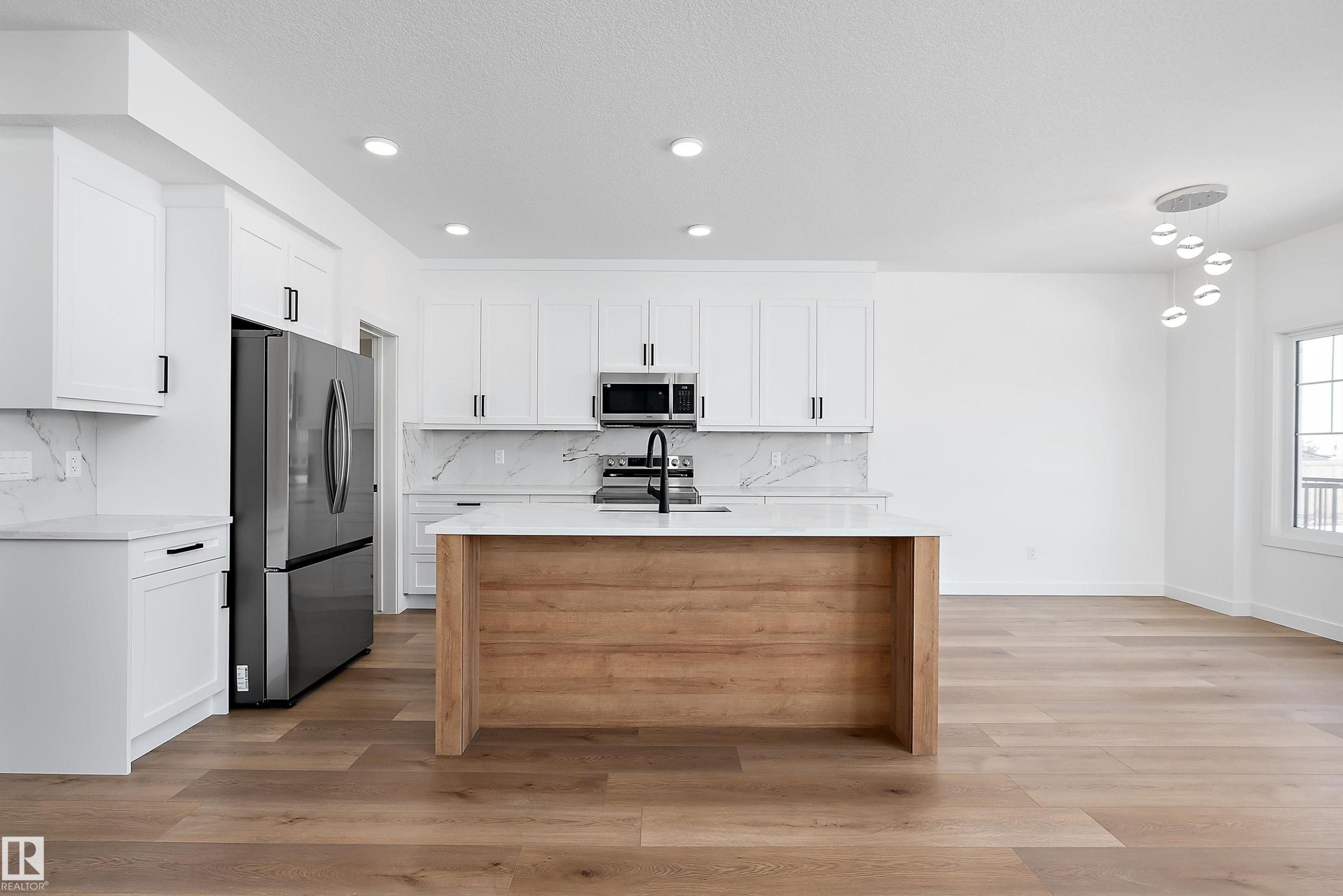 Kitchen featuring white shaker-style cabinetry, a wood-finish island with a white countertop, stainless steel appliances, and wood-finish flooring - 1763 Crossbill Loop Nw, Edmonton, AB - Indoor Photo Showing Kitchen