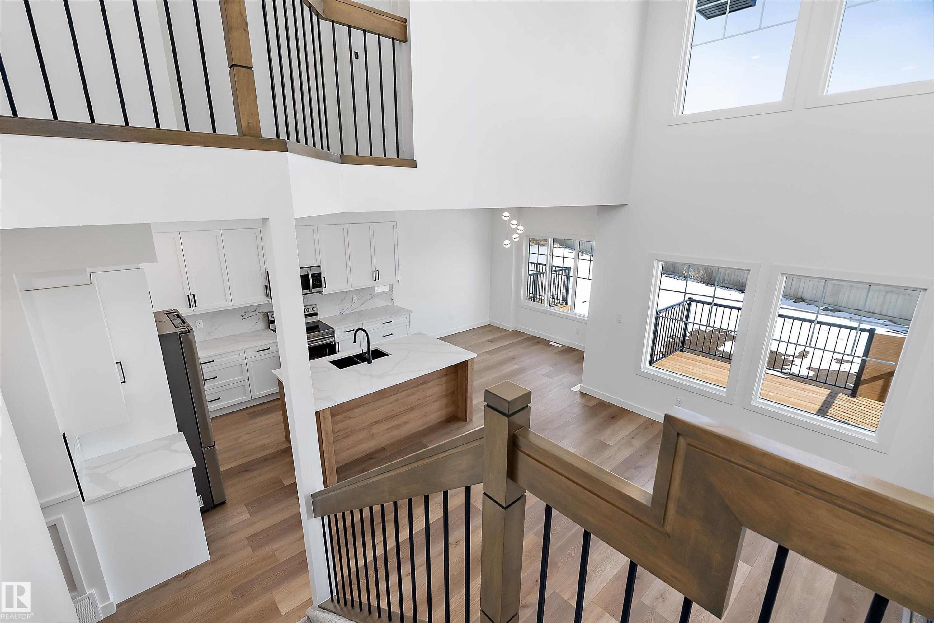 Two-story living area with high ceilings, wood-finish flooring, a contemporary kitchen, and a wooden deck - 1763 Crossbill Loop Nw, Edmonton, AB - Indoor Photo Showing Other Room