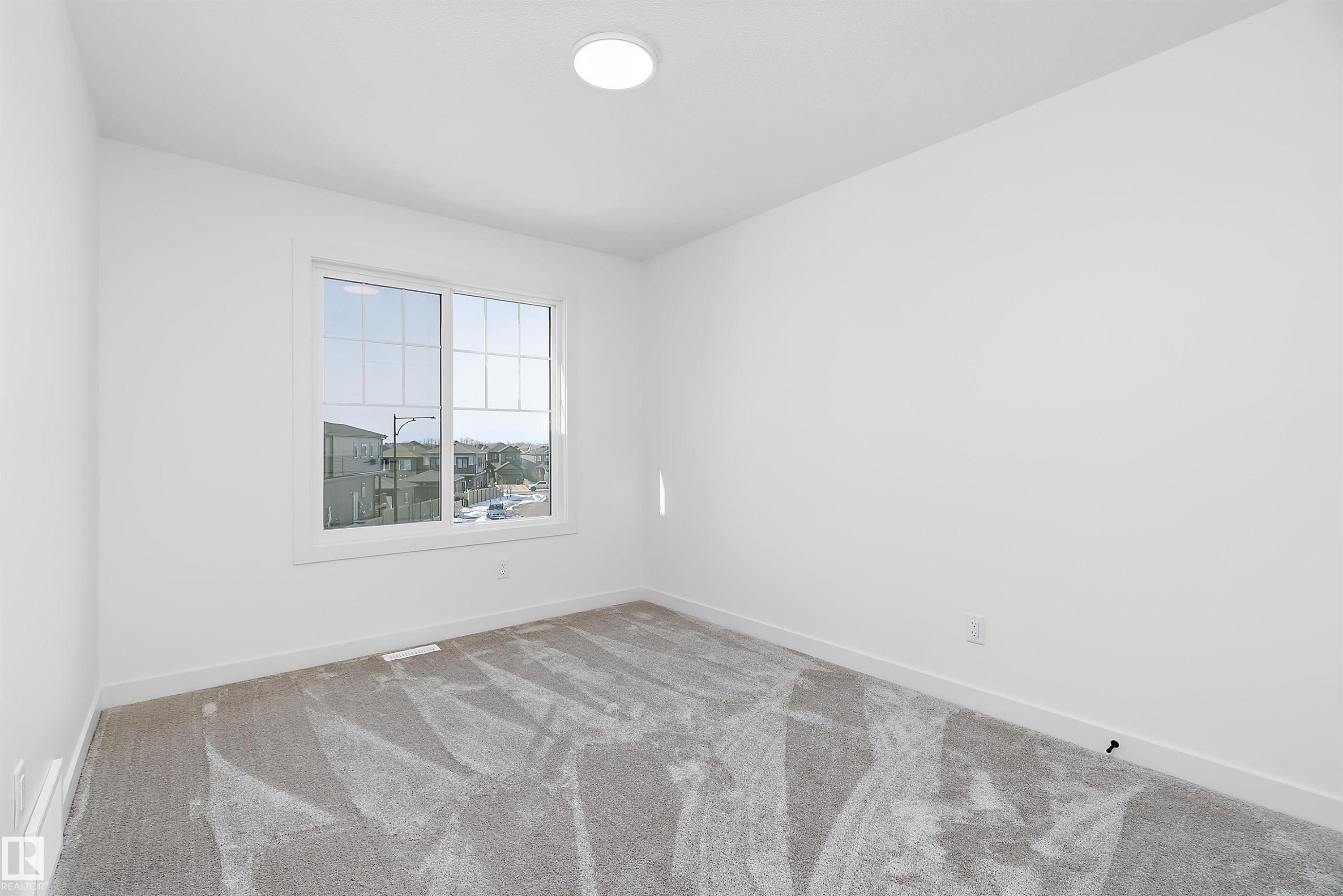 Bright room featuring a large window with multiple panes, light-colored carpeting, white walls, and a ceiling-mounted light fixture - 1763 Crossbill Loop Nw, Edmonton, AB - Indoor Photo Showing Other Room