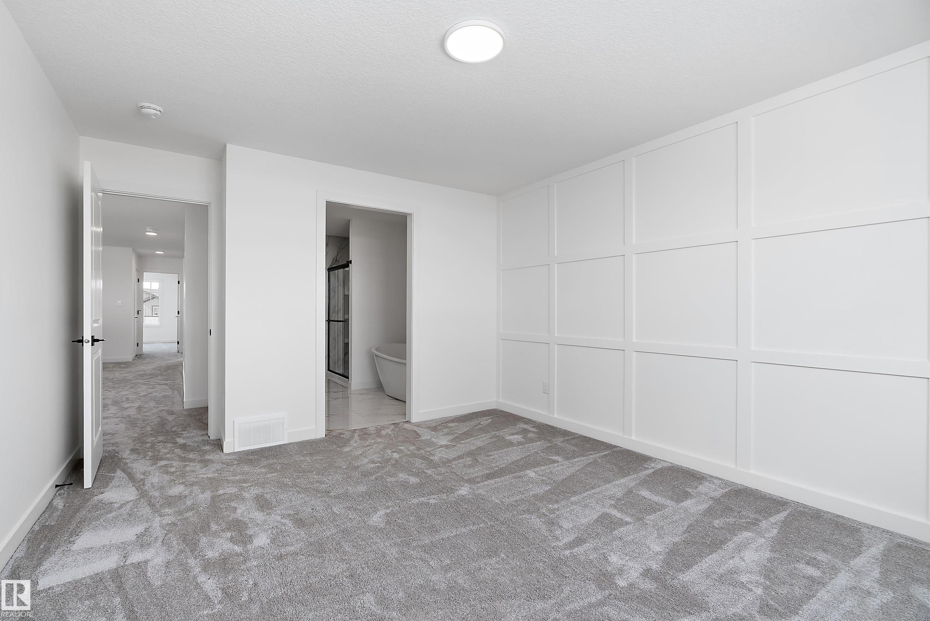 White panel accent wall, plush gray carpet, recessed lighting, white doors with matte black hardware, and a visible freestanding tub in a secondary space - 1763 Crossbill Loop Nw, Edmonton, AB - Indoor Photo Showing Other Room