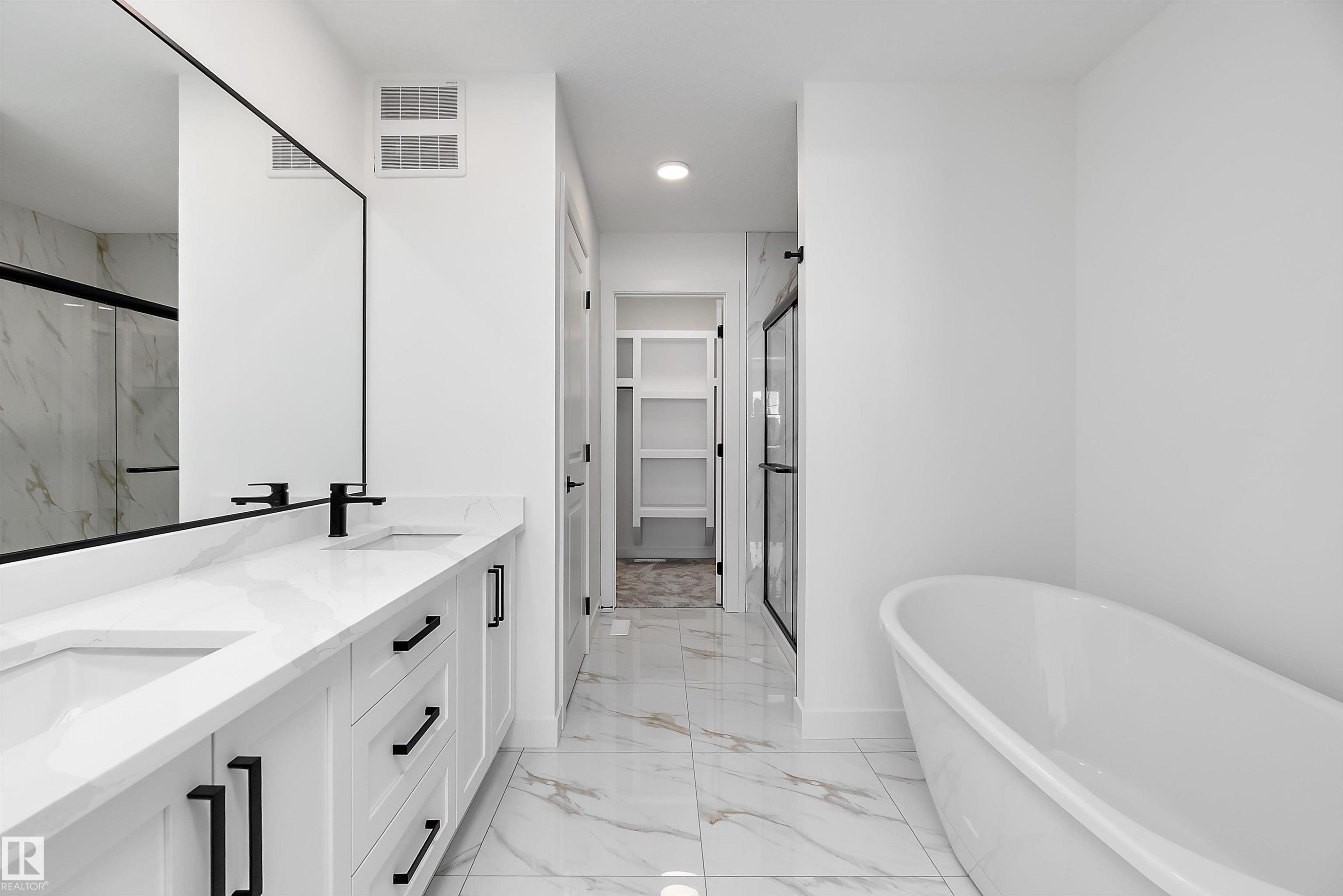 Dual vanity with white cabinetry and black hardware, freestanding soaking tub, frameless glass shower, and marble-look tile flooring - 1763 Crossbill Loop Nw, Edmonton, AB - Indoor Photo Showing Bathroom