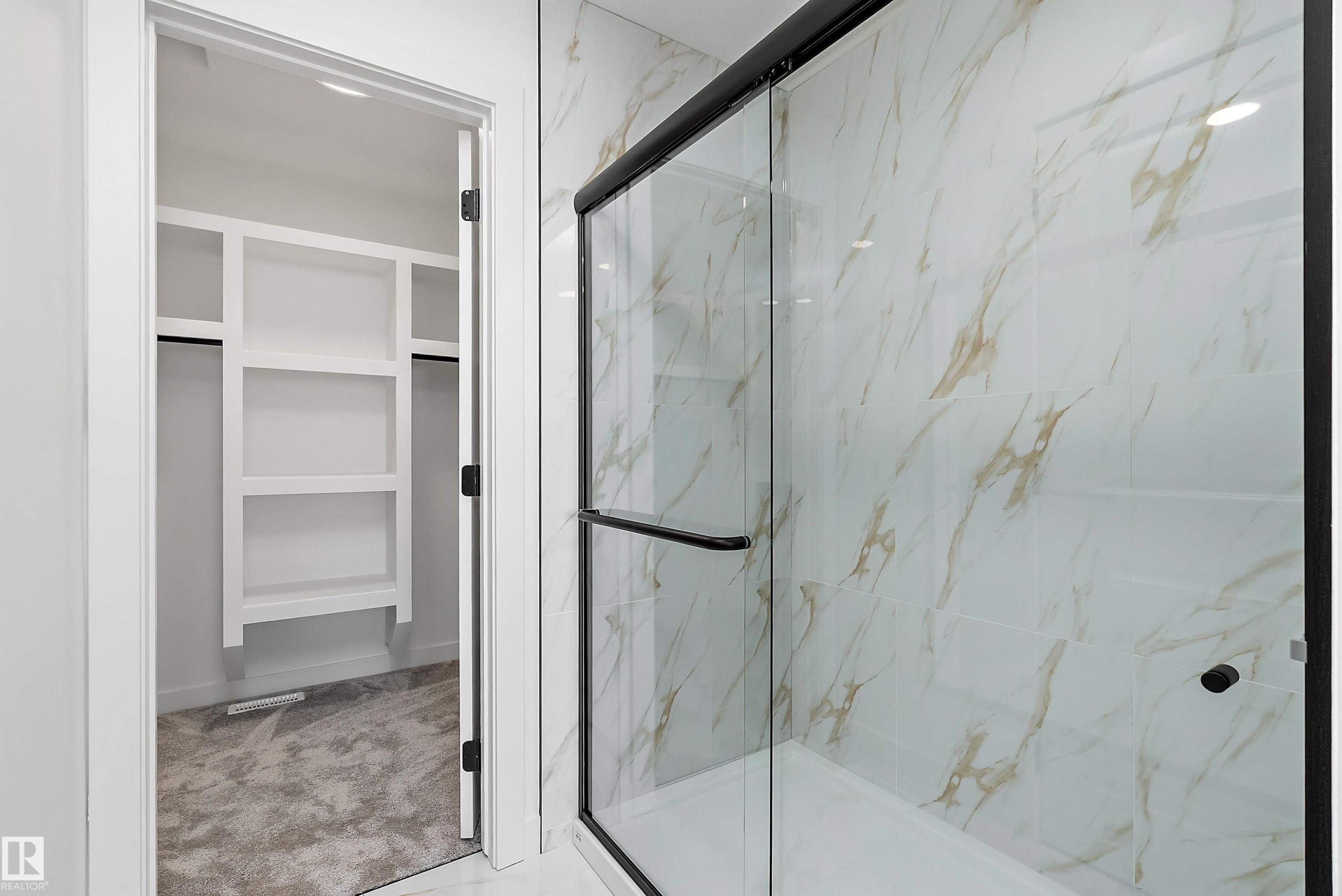 Shower enclosure with a clear glass sliding door, matte black frame, and white marble-look wall tiling - 1763 Crossbill Loop Nw, Edmonton, AB - Indoor Photo Showing Bathroom