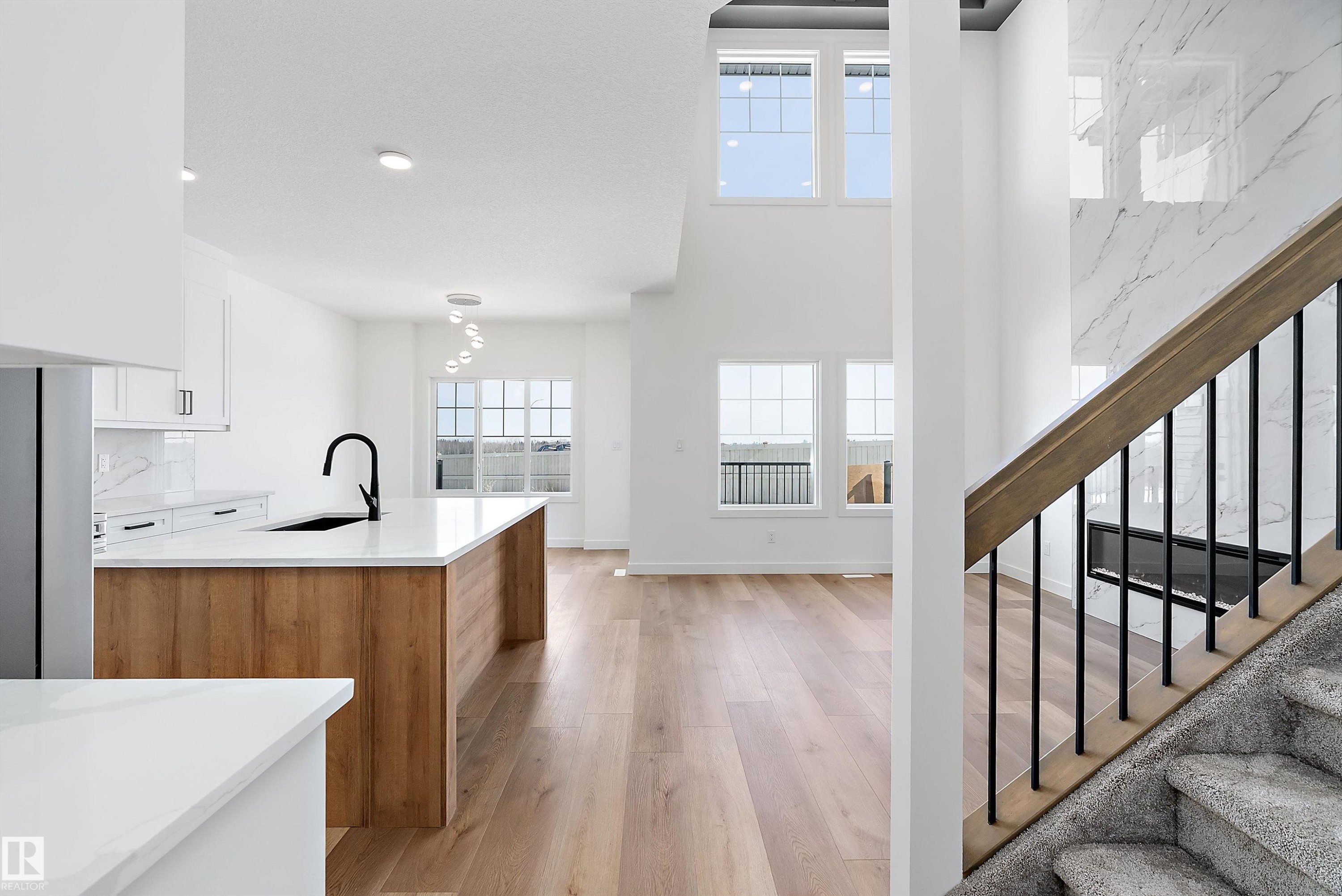Open-concept layout with light wood-finish flooring, white cabinetry, and a kitchen island featuring a black sink and faucet - 1763 Crossbill Loop Nw, Edmonton, AB - Indoor Photo Showing Kitchen