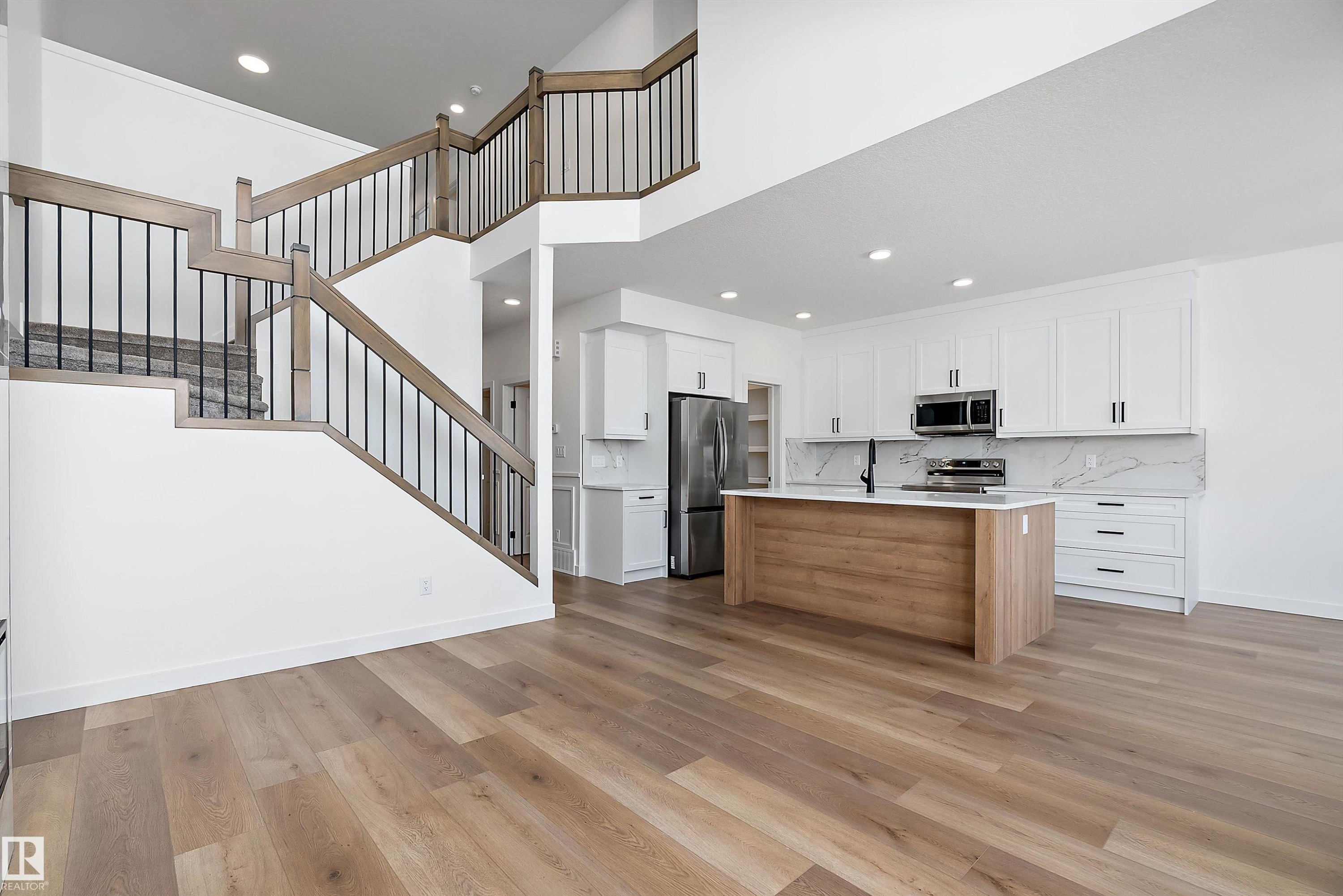 Open-concept living space with wood-finish flooring, a contemporary kitchen, and a prominent staircase with metal balusters - 1763 Crossbill Loop Nw, Edmonton, AB - Indoor Photo Showing Kitchen