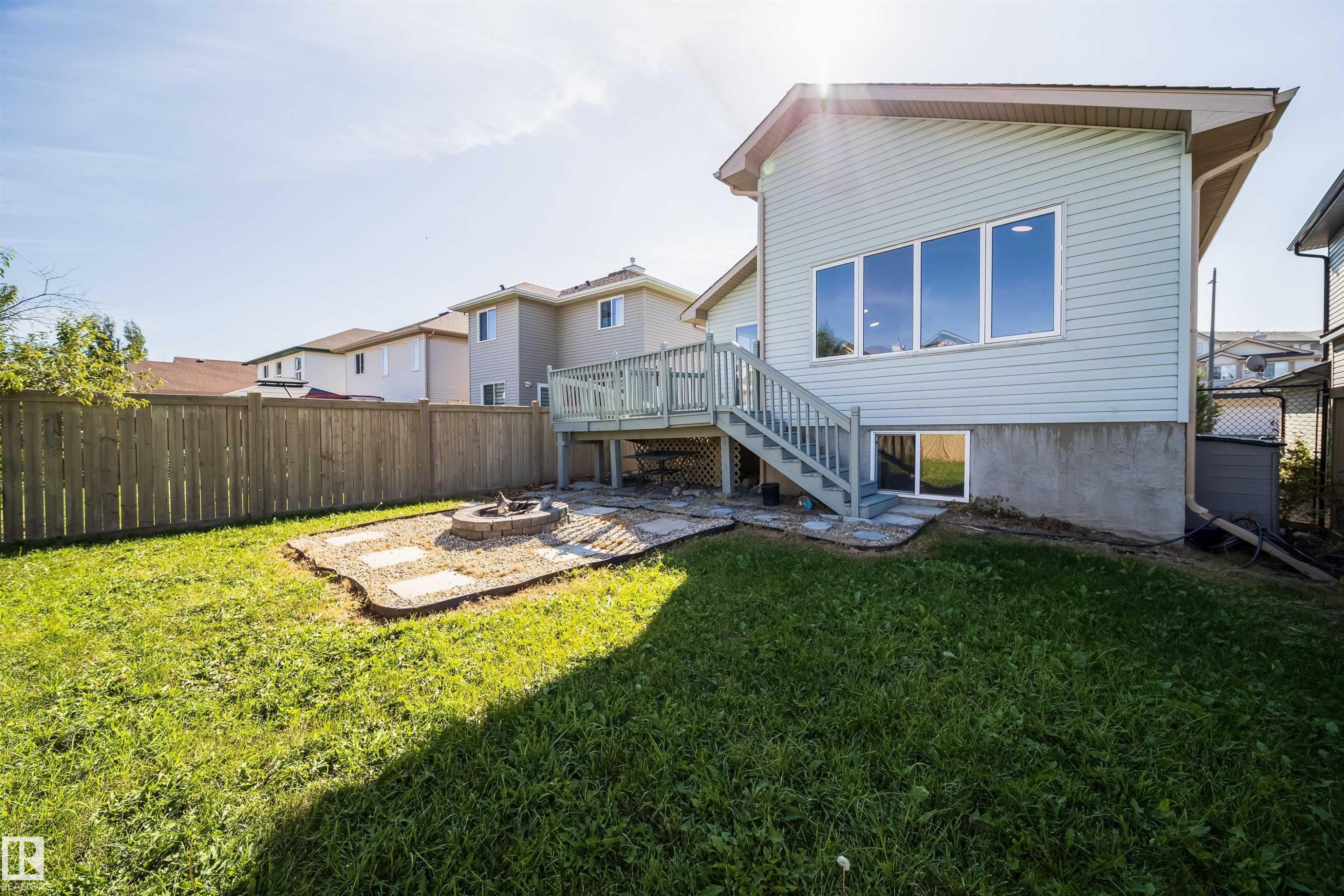 Expansive backyard featuring a wood privacy fence, a stone-bordered fire pit area, a multi-level wood deck, and a sliding glass door - 7848 7 Avenue Sw, Edmonton, AB