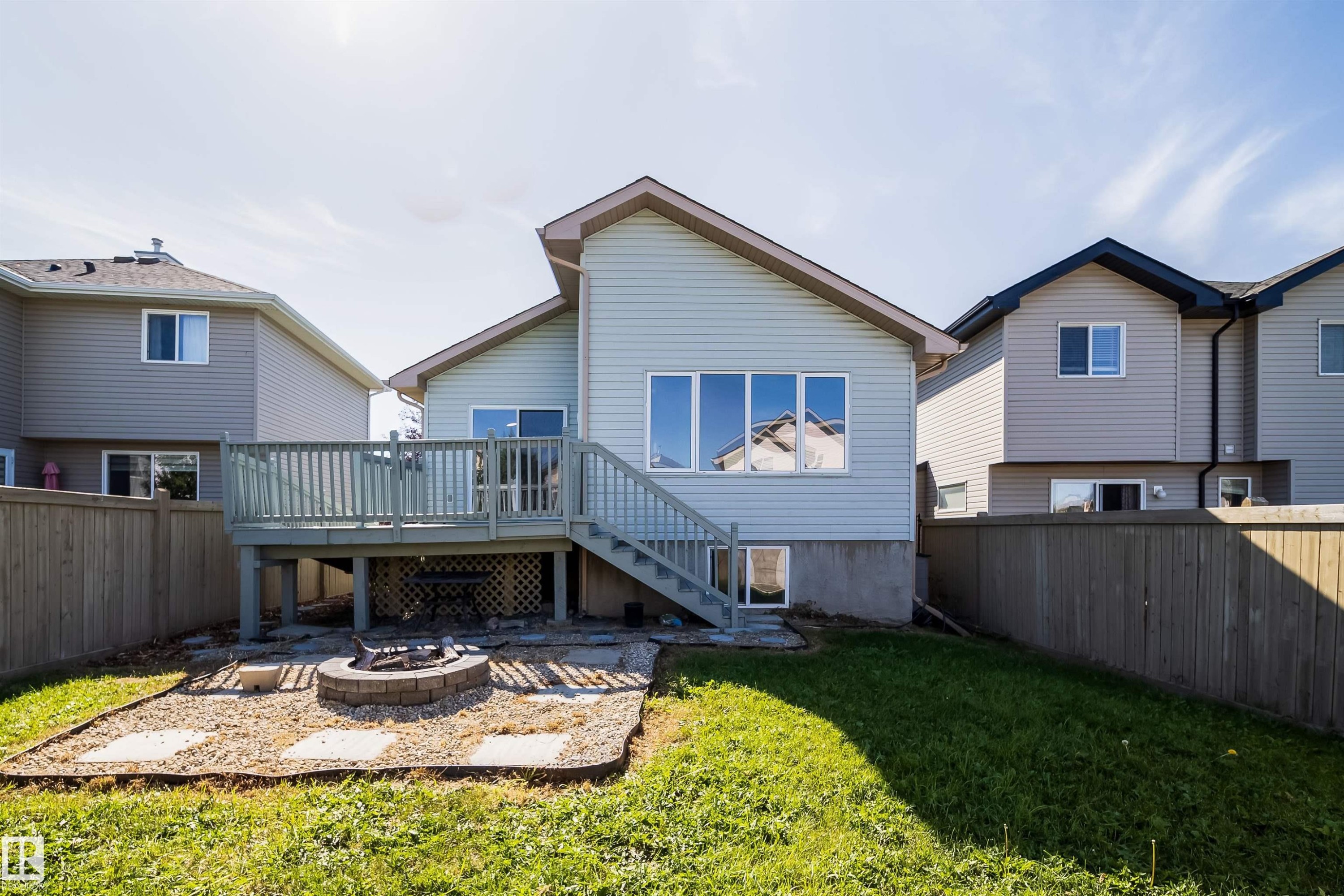 Rear exterior with a wood deck, fenced yard, and a stone fire pit area - 7848 7 Avenue Sw, Edmonton, AB