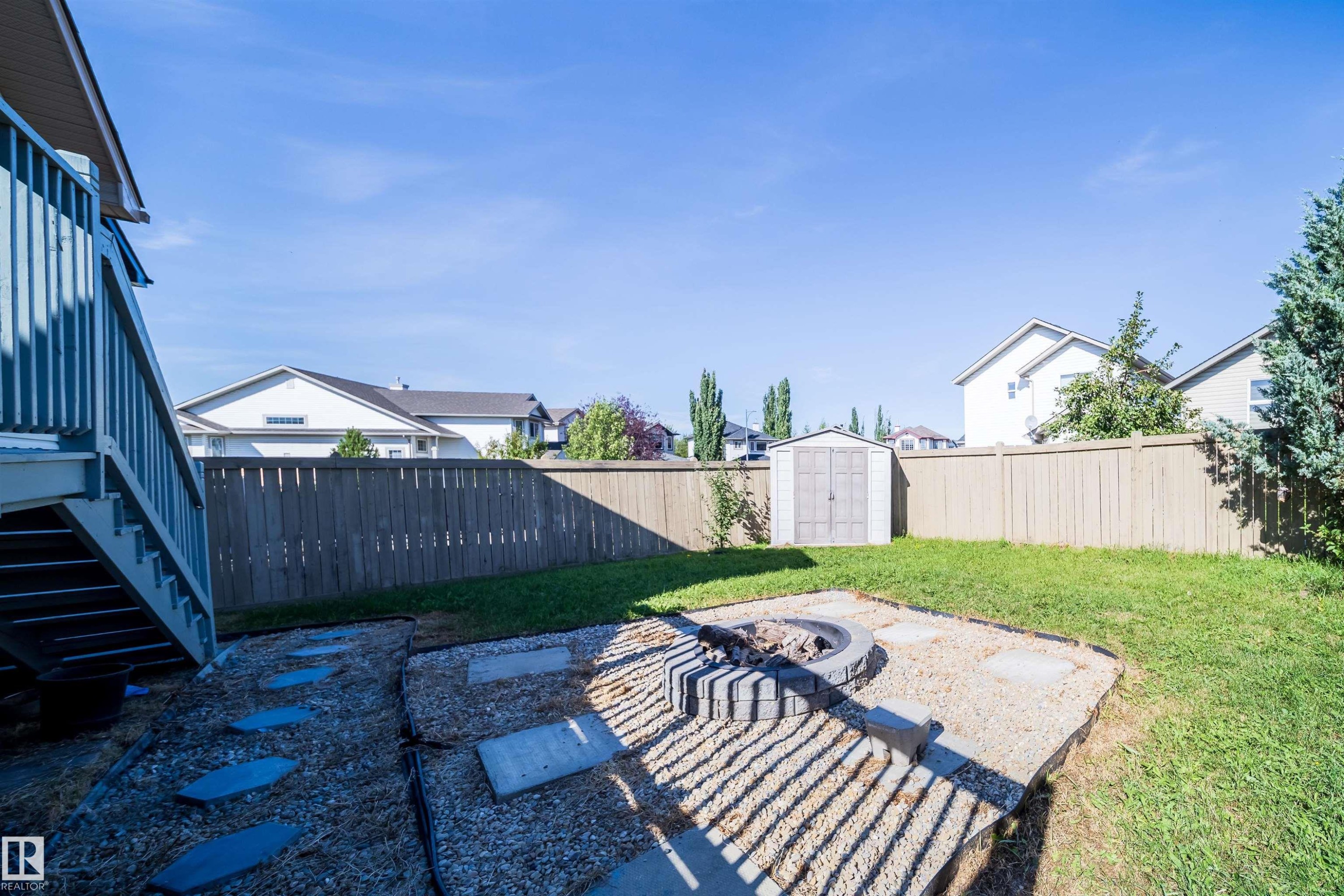 Expansive backyard featuring a wood privacy fence, a built-in fire pit area with gravel, a storage shed, and a wooden deck with stairs - 7848 7 Avenue Sw, Edmonton, AB
