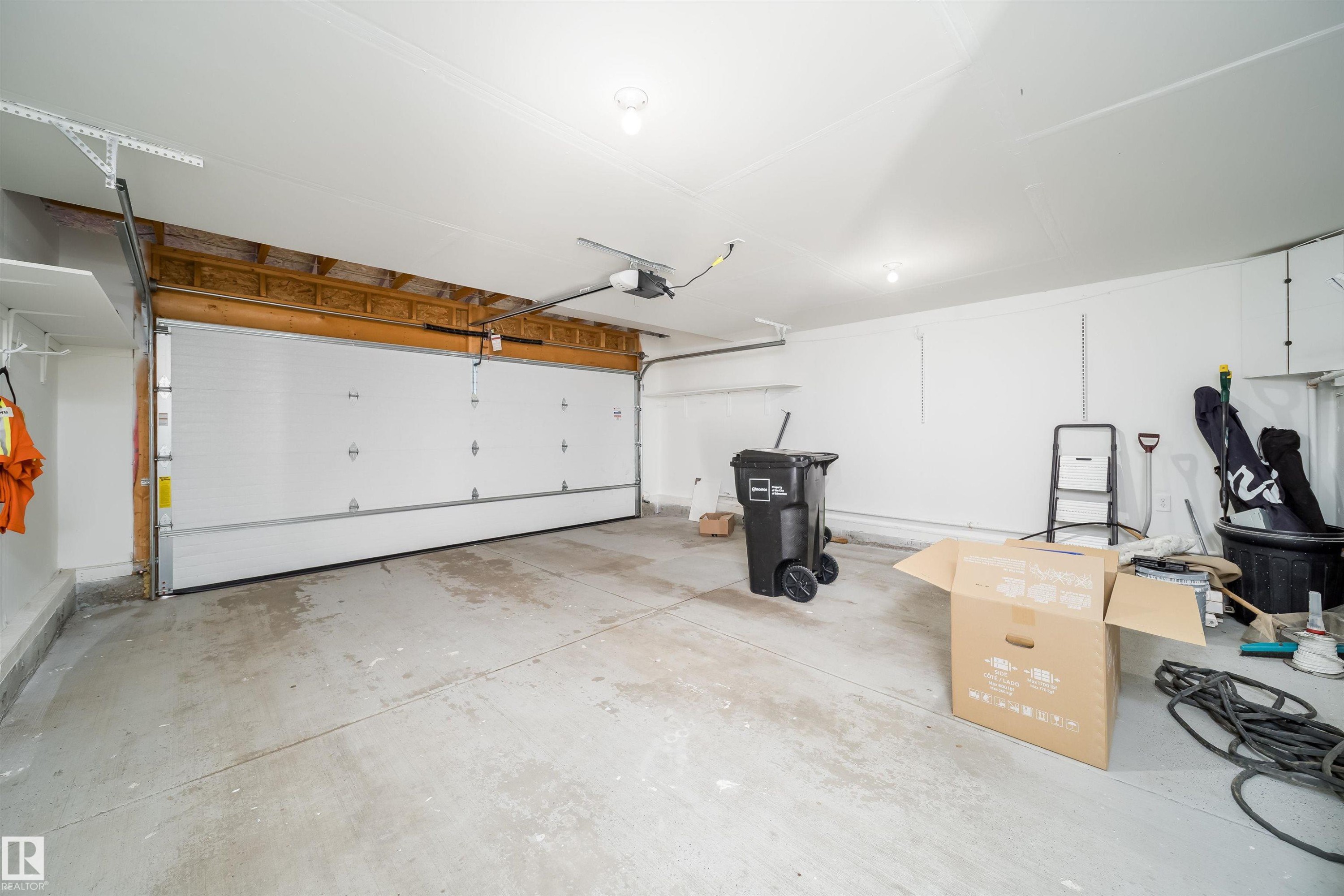 Concrete flooring and white walls, featuring a sectional garage door with an automatic opener - 7848 7 Avenue Sw, Edmonton, AB