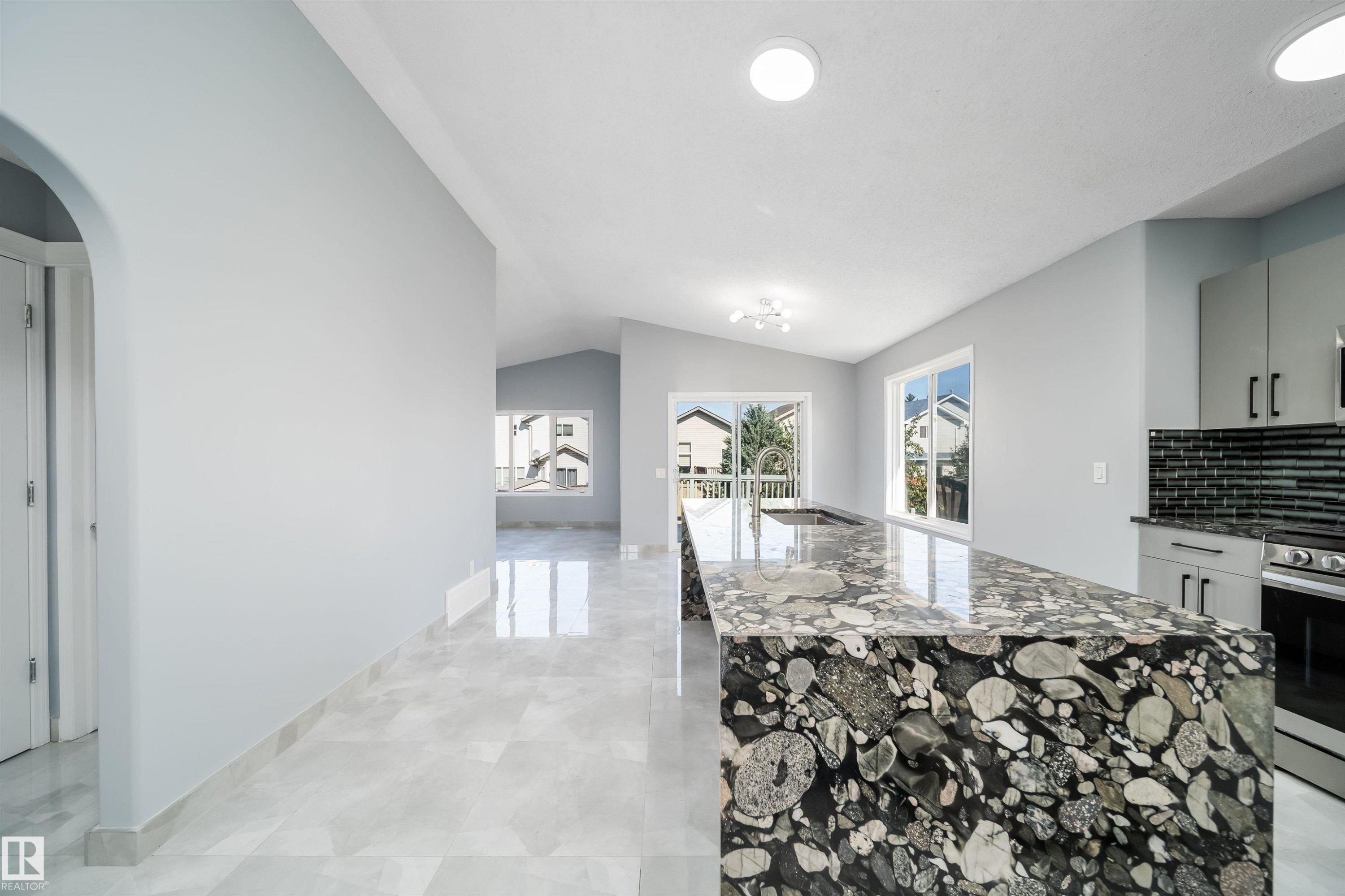 Spacious kitchen island with unique stone countertop, integrated sink, and modern cabinetry - 7848 7 Avenue Sw, Edmonton, AB