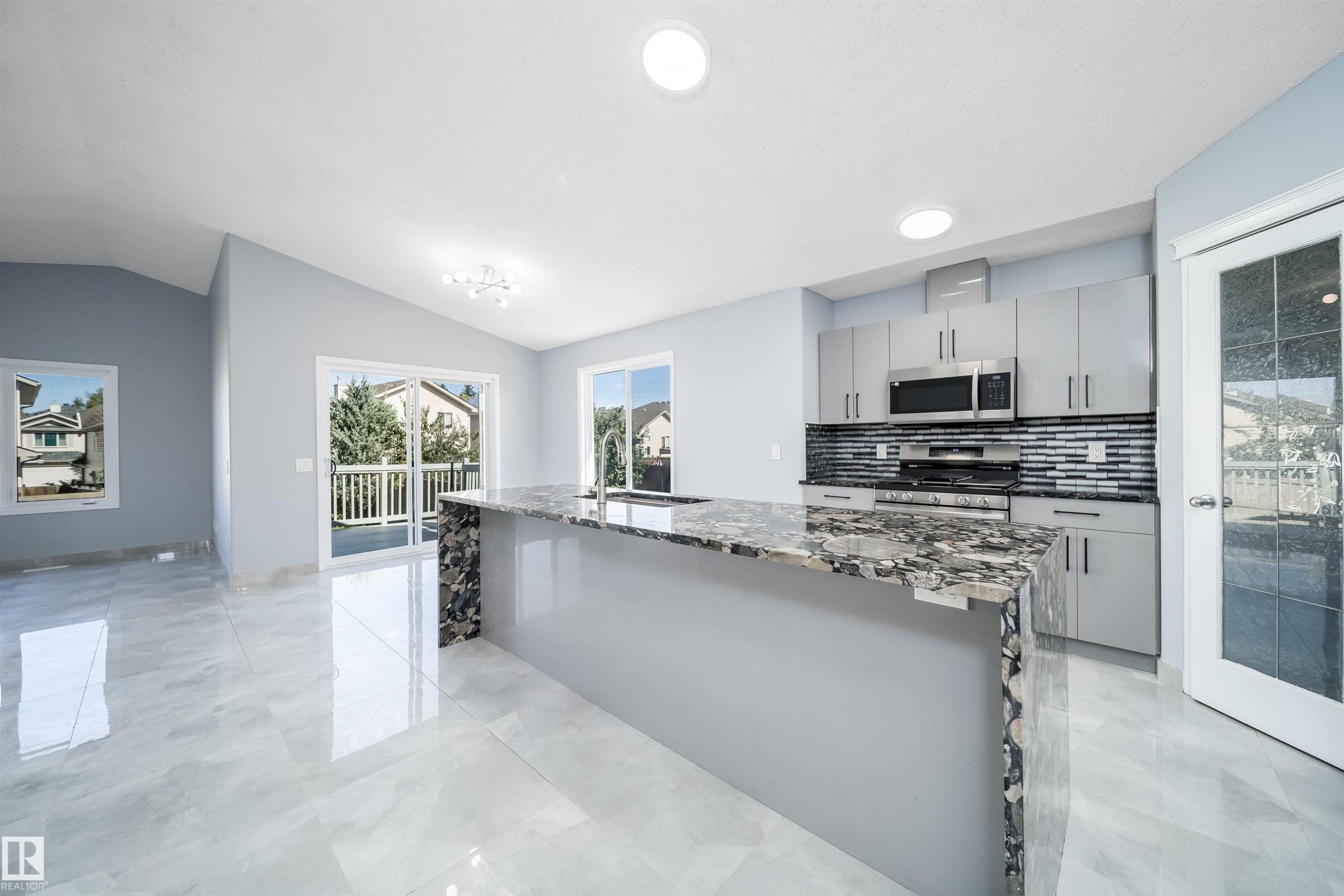 Kitchen featuring a central island with a stone countertop, stainless steel appliances, modern cabinetry, and a tile backsplash - 7848 7 Avenue Sw, Edmonton, AB