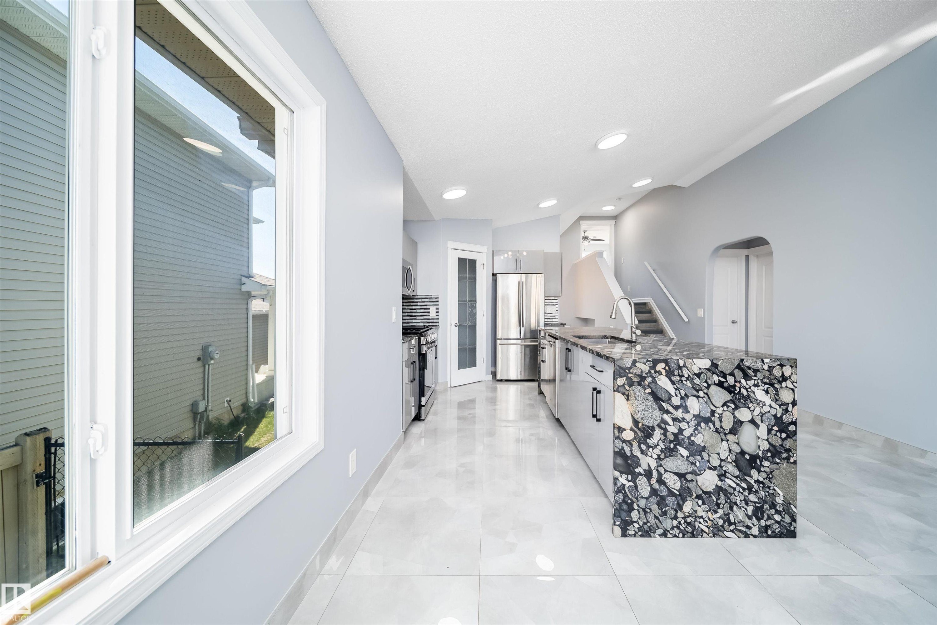 Expansive kitchen island with a unique stone countertop, stainless steel appliances, recessed ceiling lighting, and light-toned tile flooring - 7848 7 Avenue Sw, Edmonton, AB