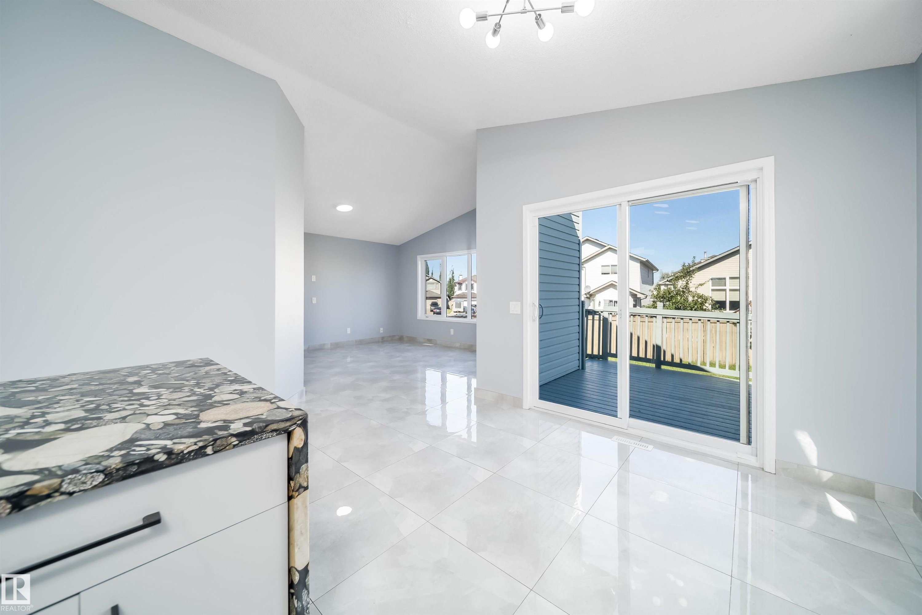 Sliding glass door to an outdoor deck, vaulted ceilings, recessed lighting, large window, and light-colored tile flooring - 7848 7 Avenue Sw, Edmonton, AB