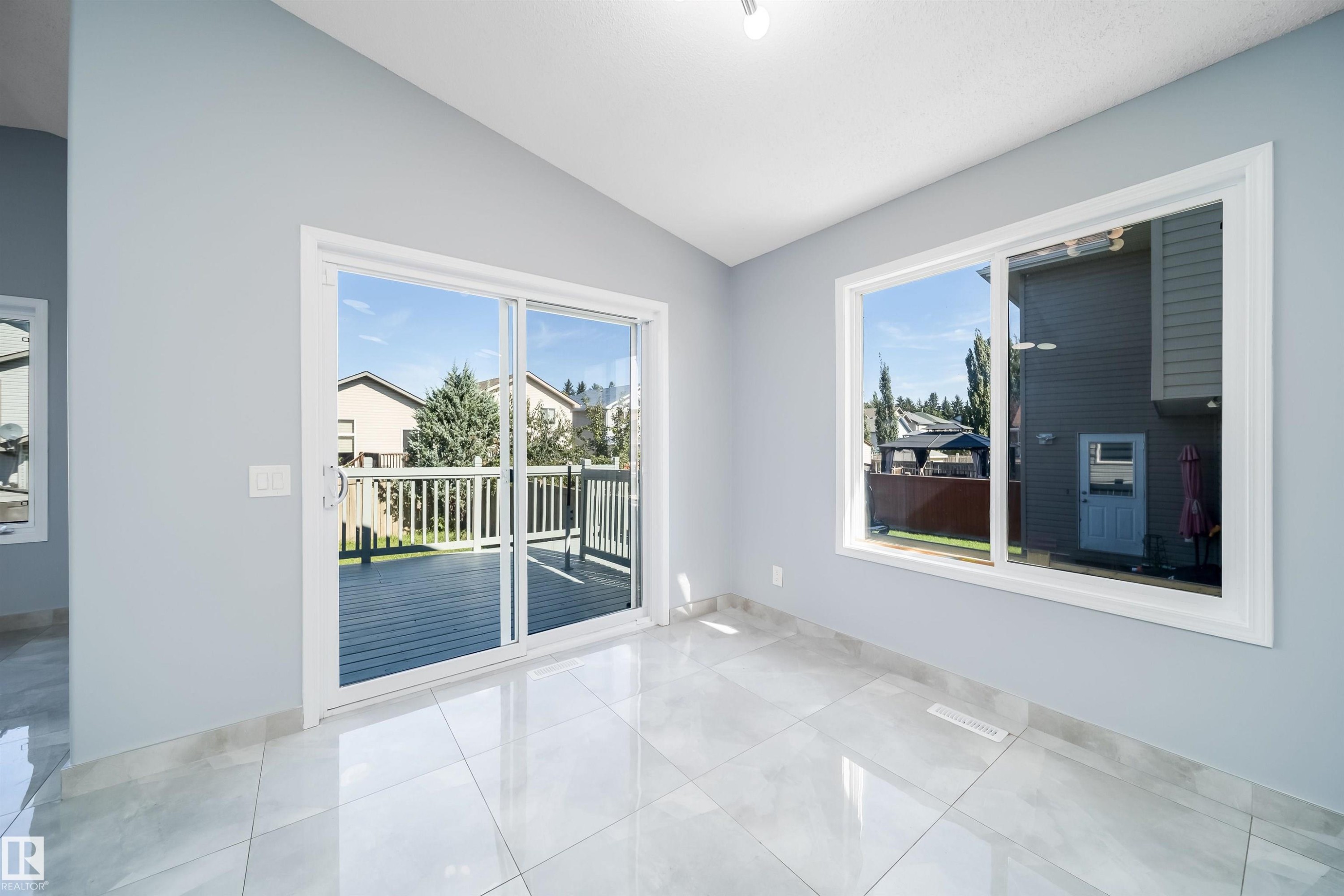 Glossy tile flooring, white trim, sliding glass door with exterior deck, large window, and vaulted ceiling - 7848 7 Avenue Sw, Edmonton, AB