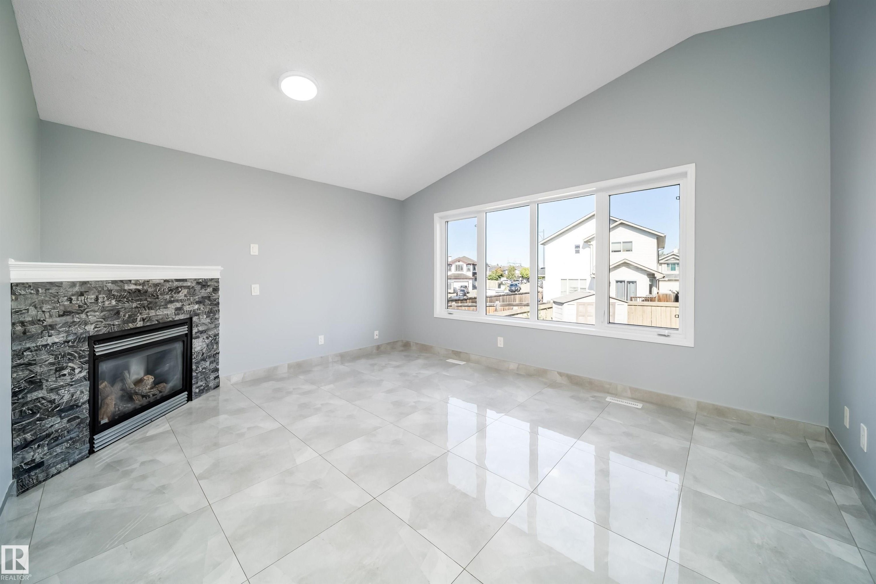 Vaulted ceiling with recessed lighting, large pane windows, stone-clad fireplace with mantel, and tile flooring - 7848 7 Avenue Sw, Edmonton, AB
