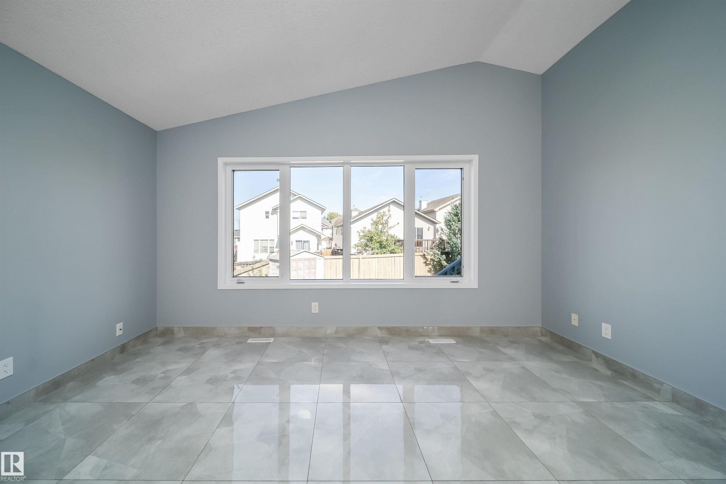 Vaulted ceiling, expansive window with white trim, light-toned wall finish, and large format tile flooring - 7848 7 Avenue Sw, Edmonton, AB