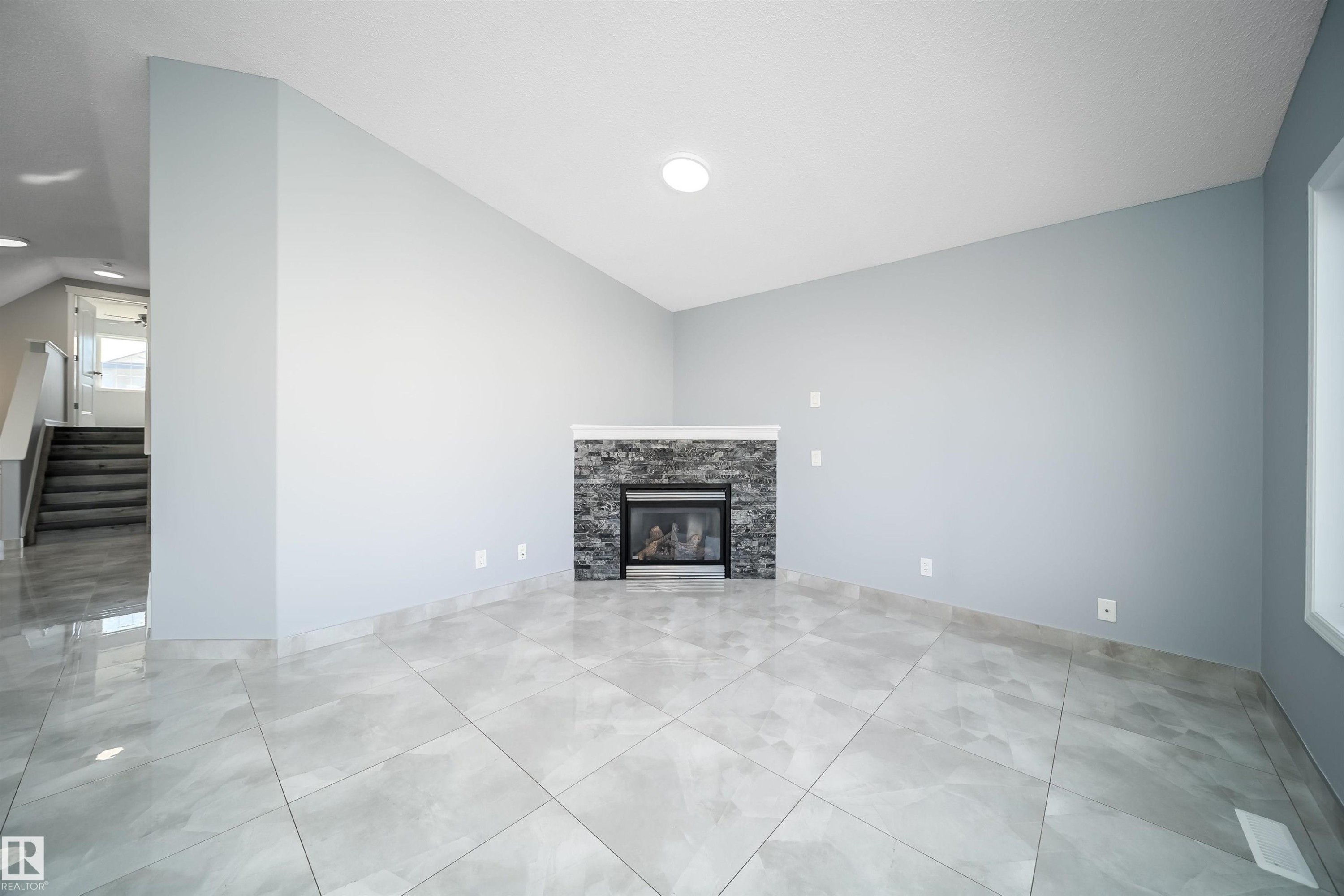 Vaulted ceiling, recessed lighting, tile flooring, stone-clad fireplace, and a large window - 7848 7 Avenue Sw, Edmonton, AB